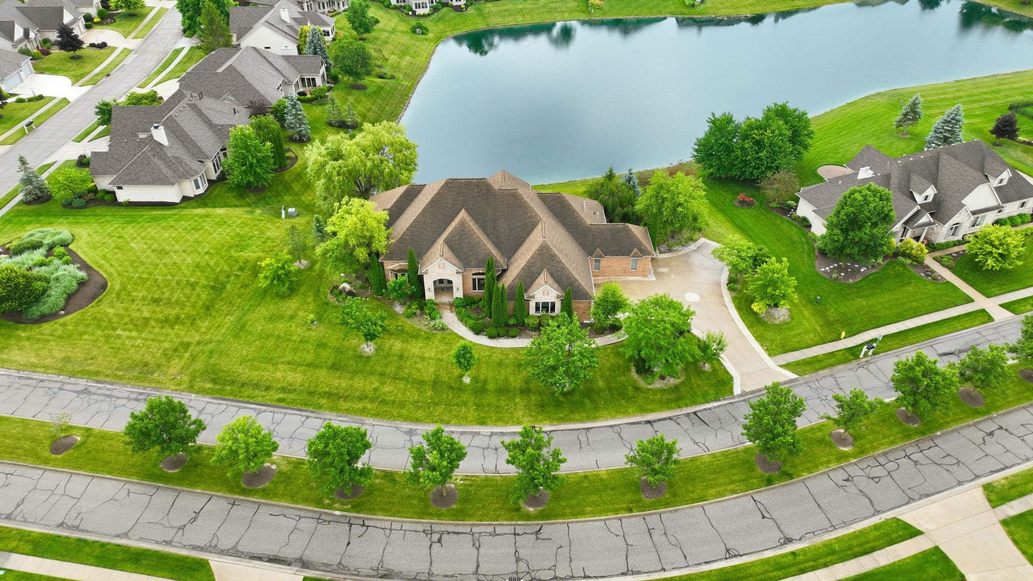 Residential property featuring a large body of water, extensive green lawns, mature trees, and a curved street