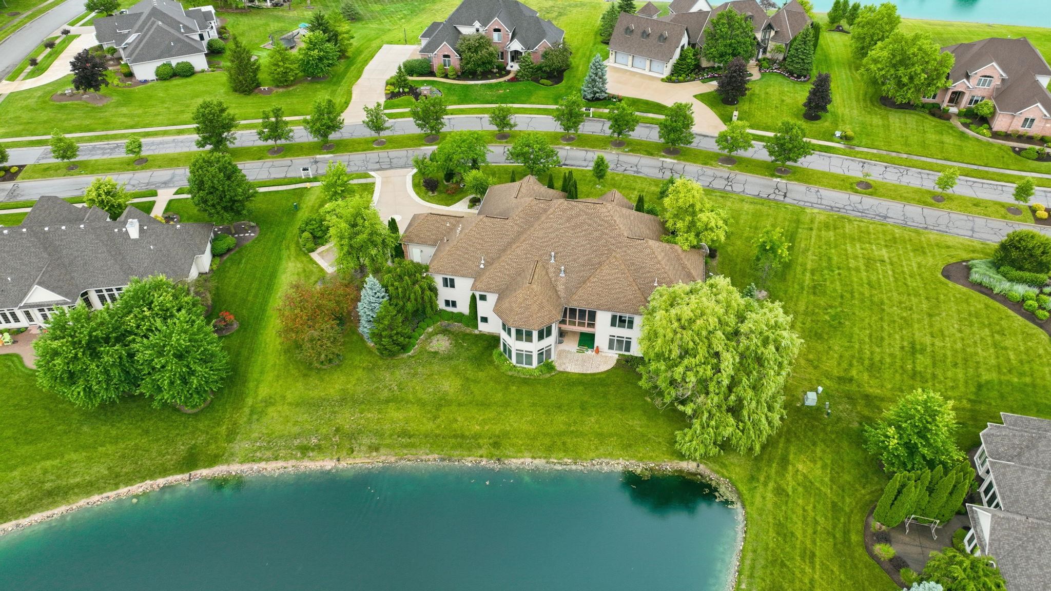 Lakeside property featuring a multi-story residence with a tan roof, white exterior, and expansive green lawns