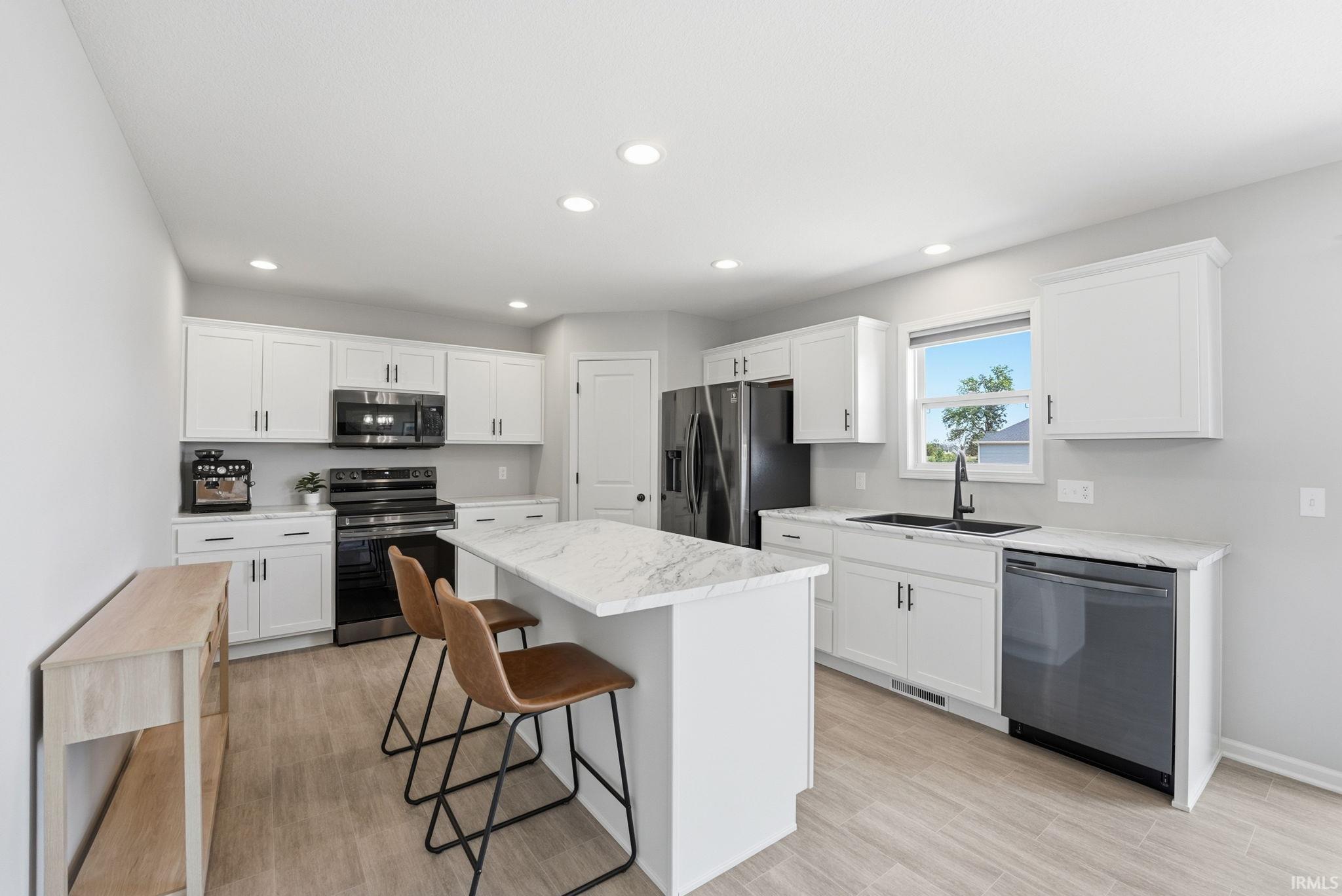Modern kitchen featuring white cabinetry, black appliances, recessed lighting, a central island with countertop seating, and light wood-finish flooring