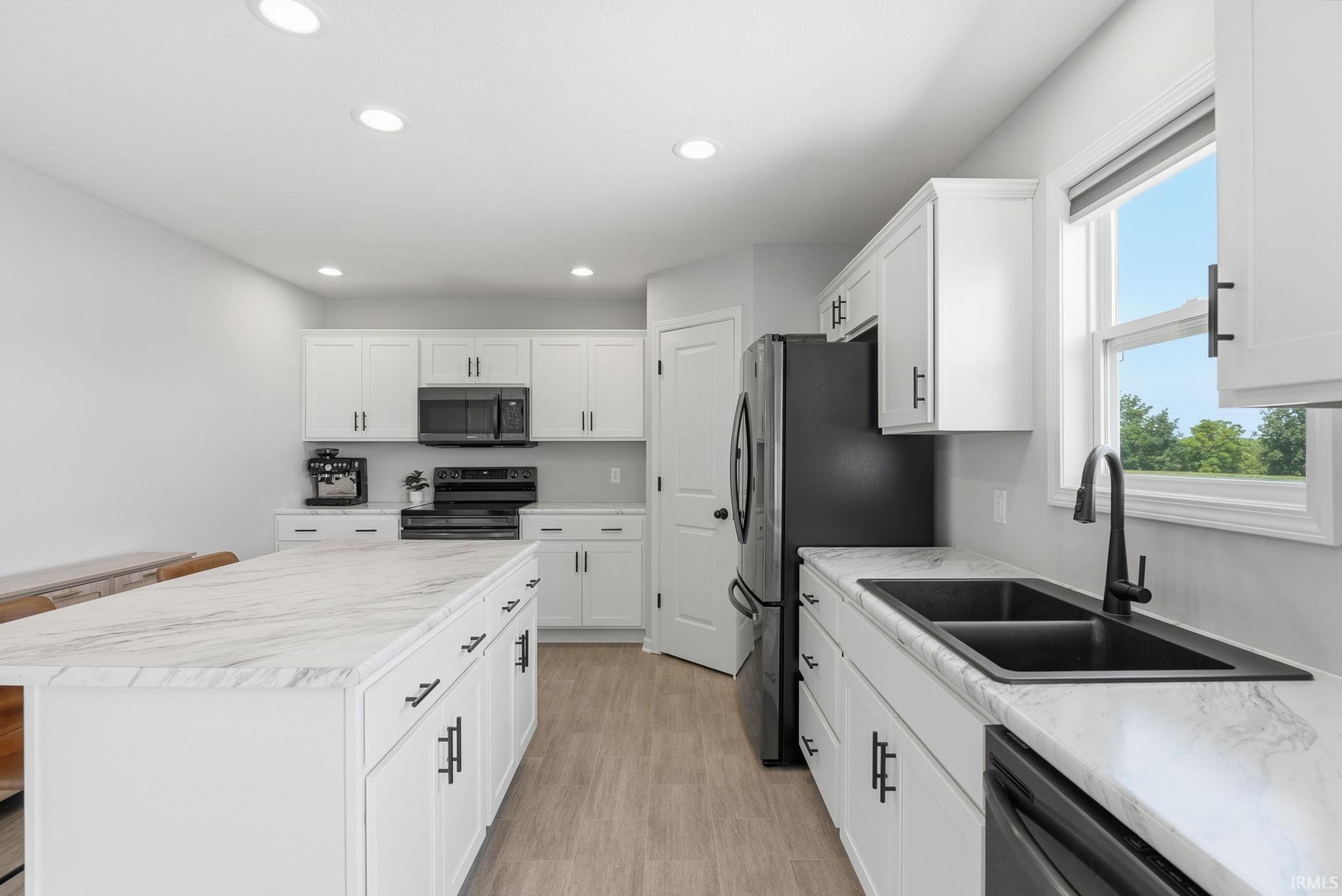 Kitchen featuring white shaker-style cabinetry, light-toned wood-finish flooring, a double basin sink with a matte black faucet, integrated dishwasher, and recessed lighting