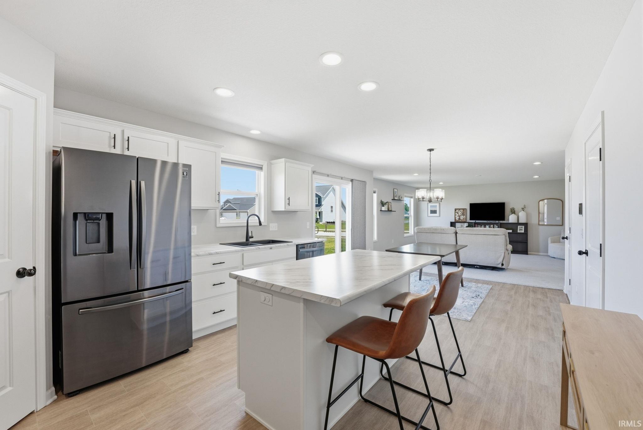 Open-concept kitchen featuring an eat-at island with a light-toned countertop, white cabinetry, a black appliance suite, and wood-finish flooring