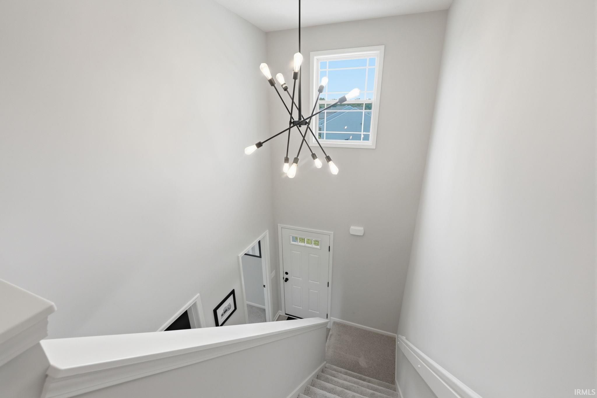 Two-story entryway featuring a modern linear chandelier, high ceilings, and a transom window