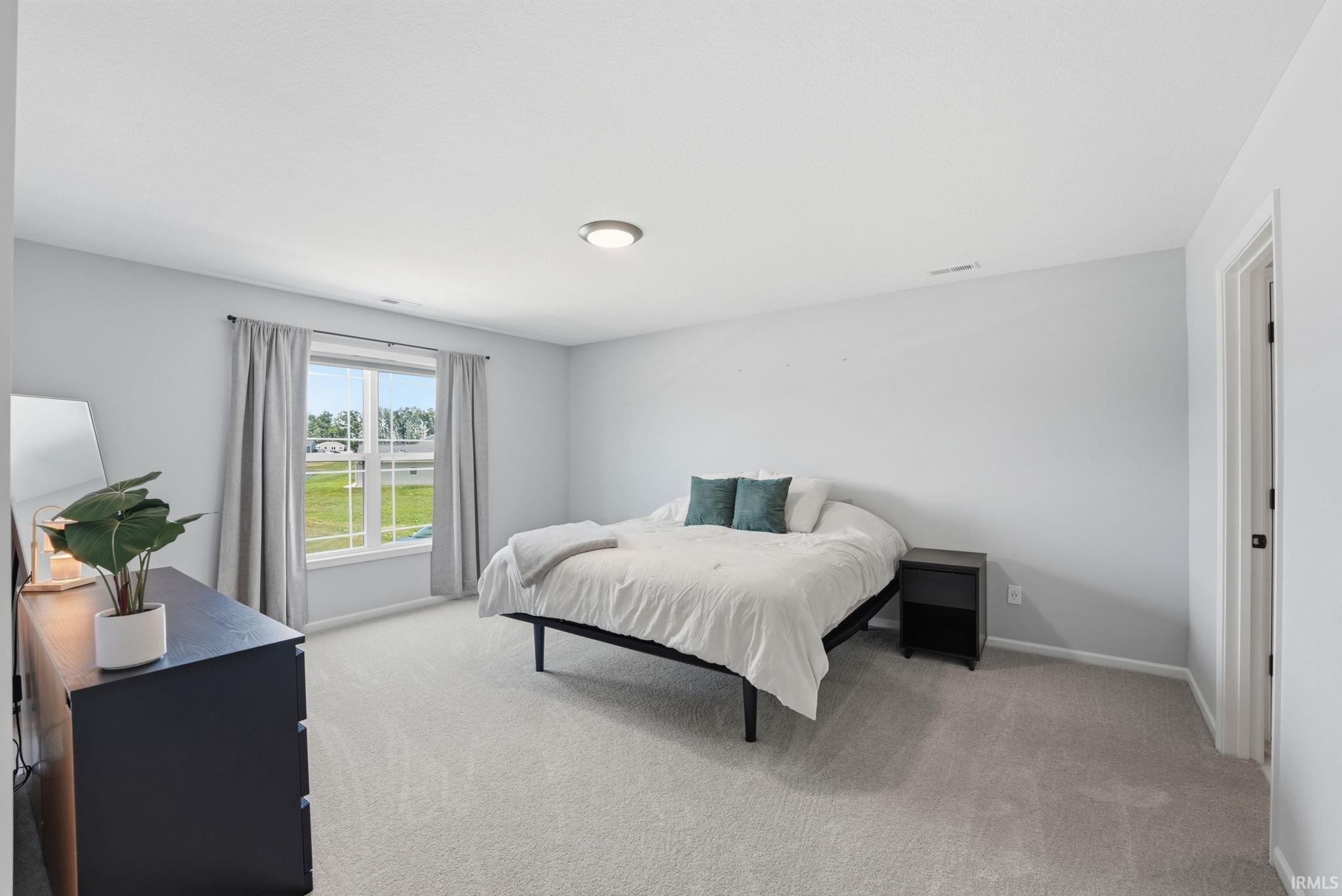 Spacious room featuring light gray wall paint, light gray carpeting, and a ceiling-mounted light fixture