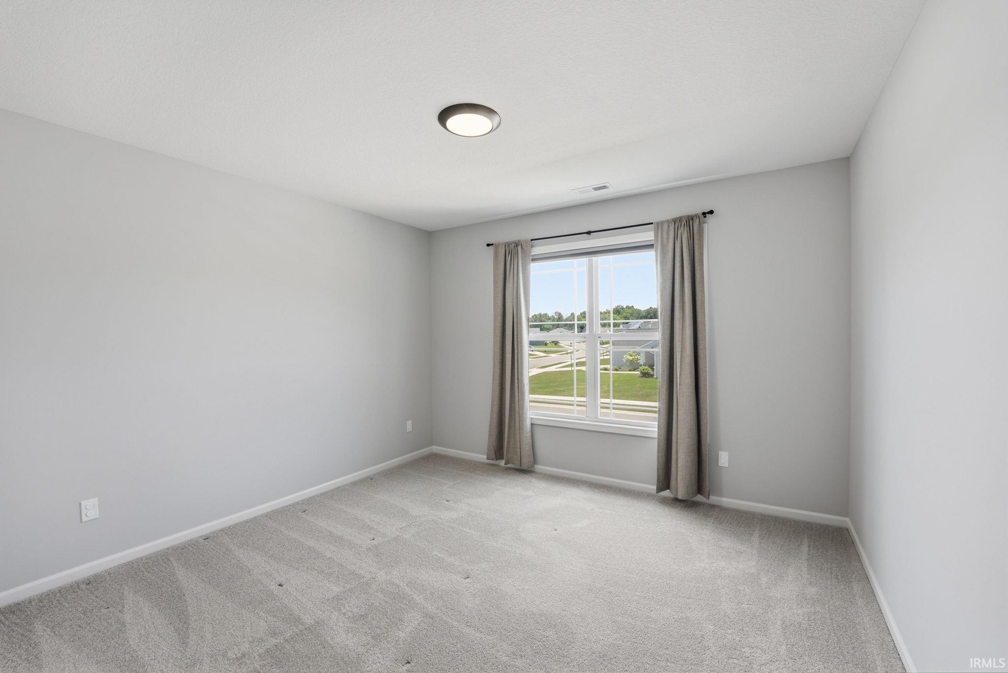 Neutral-toned room featuring a window with white trim, light gray walls, plush gray carpet, and a flush-mount ceiling light