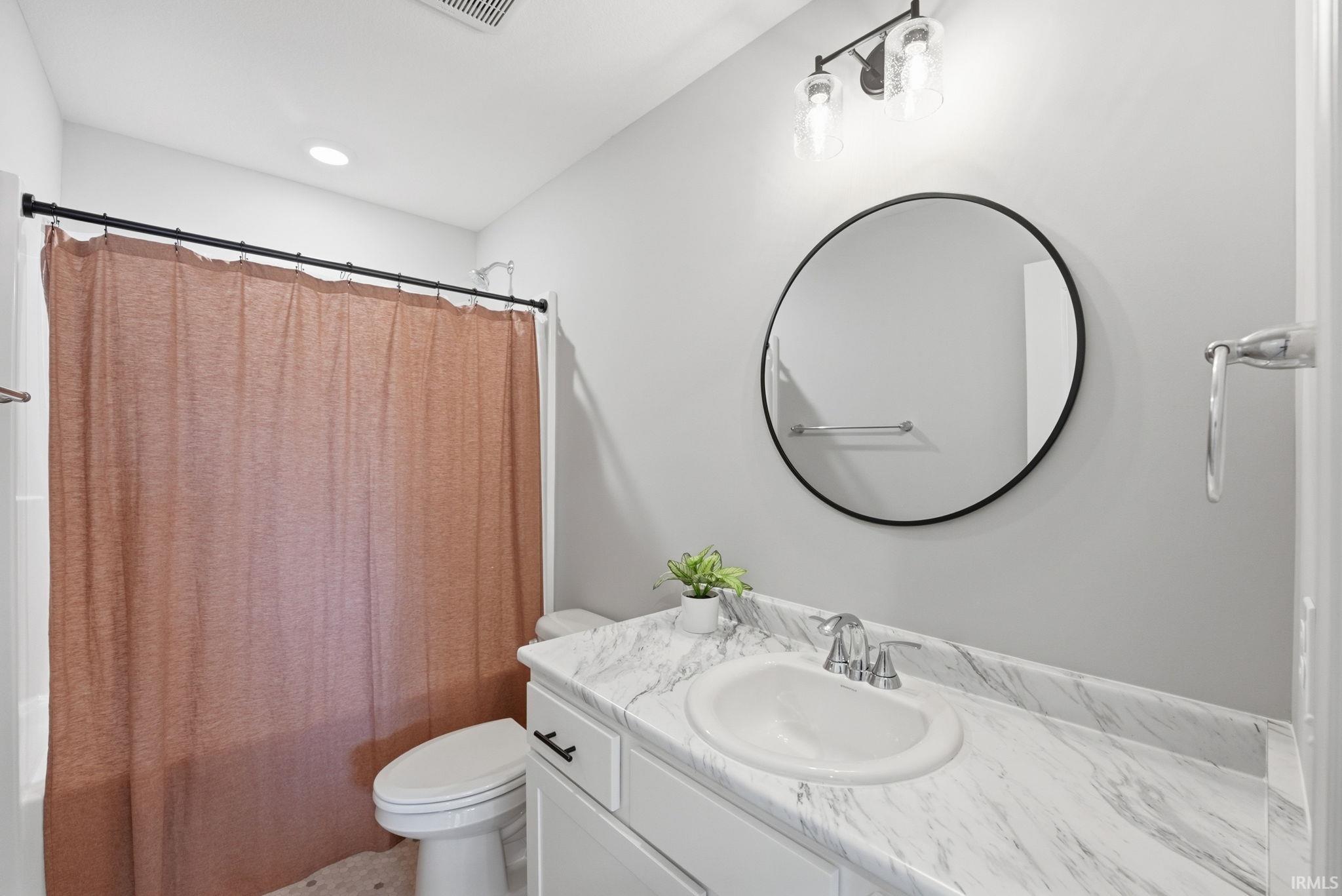 Bathroom featuring a white vanity with a patterned countertop, an undermount sink, and a circular mirror