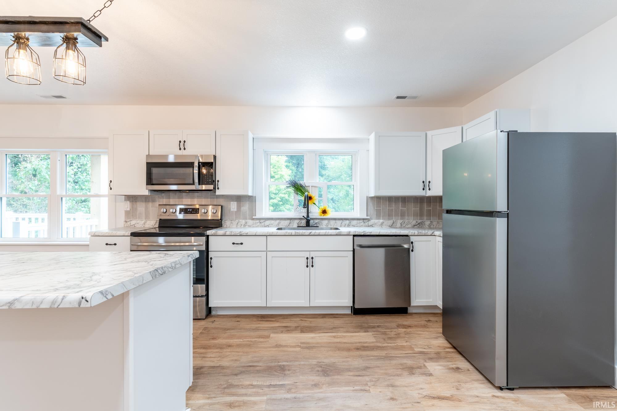 Kitchen featuring wood-finish flooring, white cabinetry with dark hardware, stainless steel appliances, and light-toned countertops