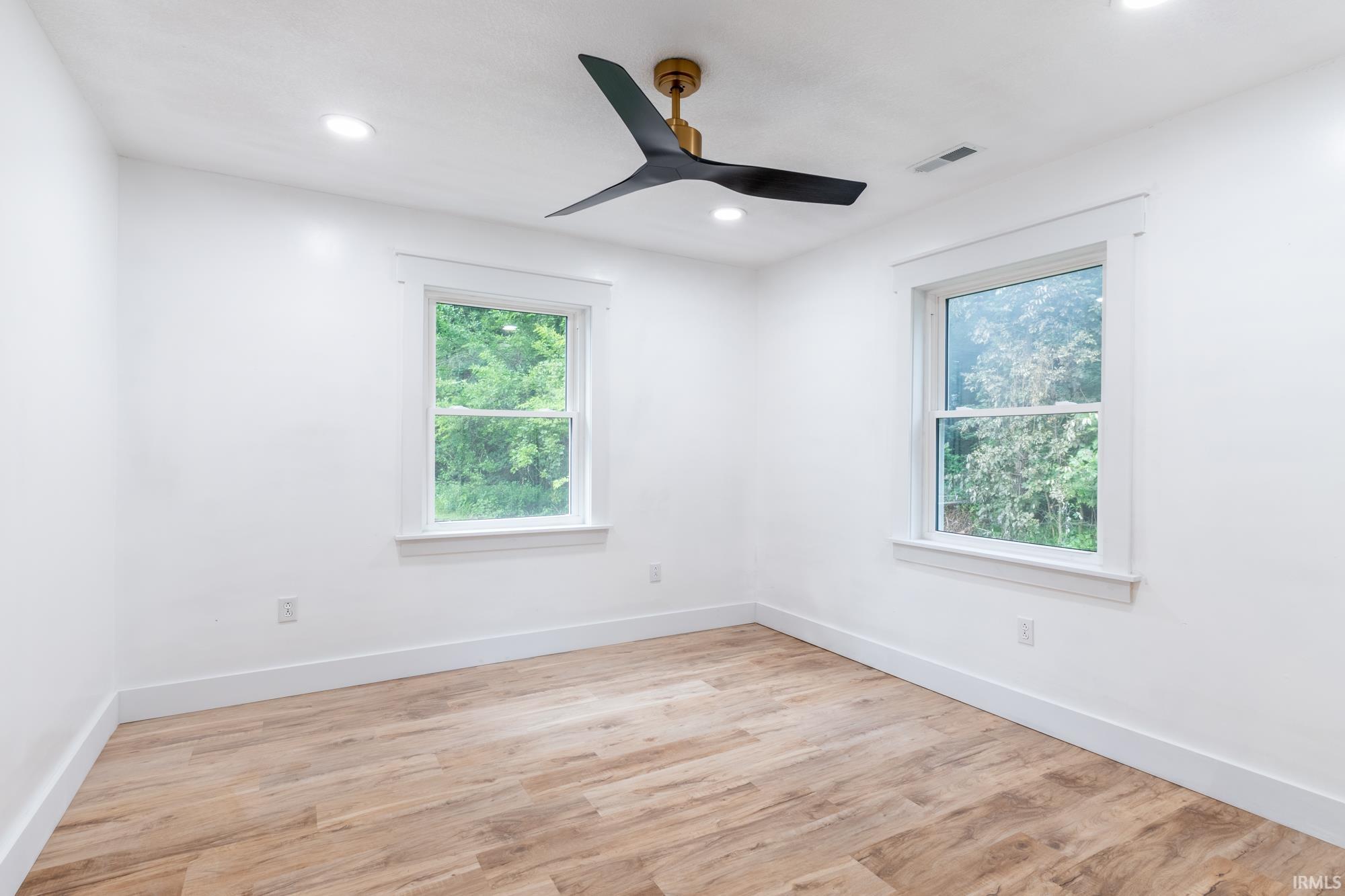 Room featuring wood-finish flooring, white walls, and a contemporary ceiling fan with black blades and a brass-tone base