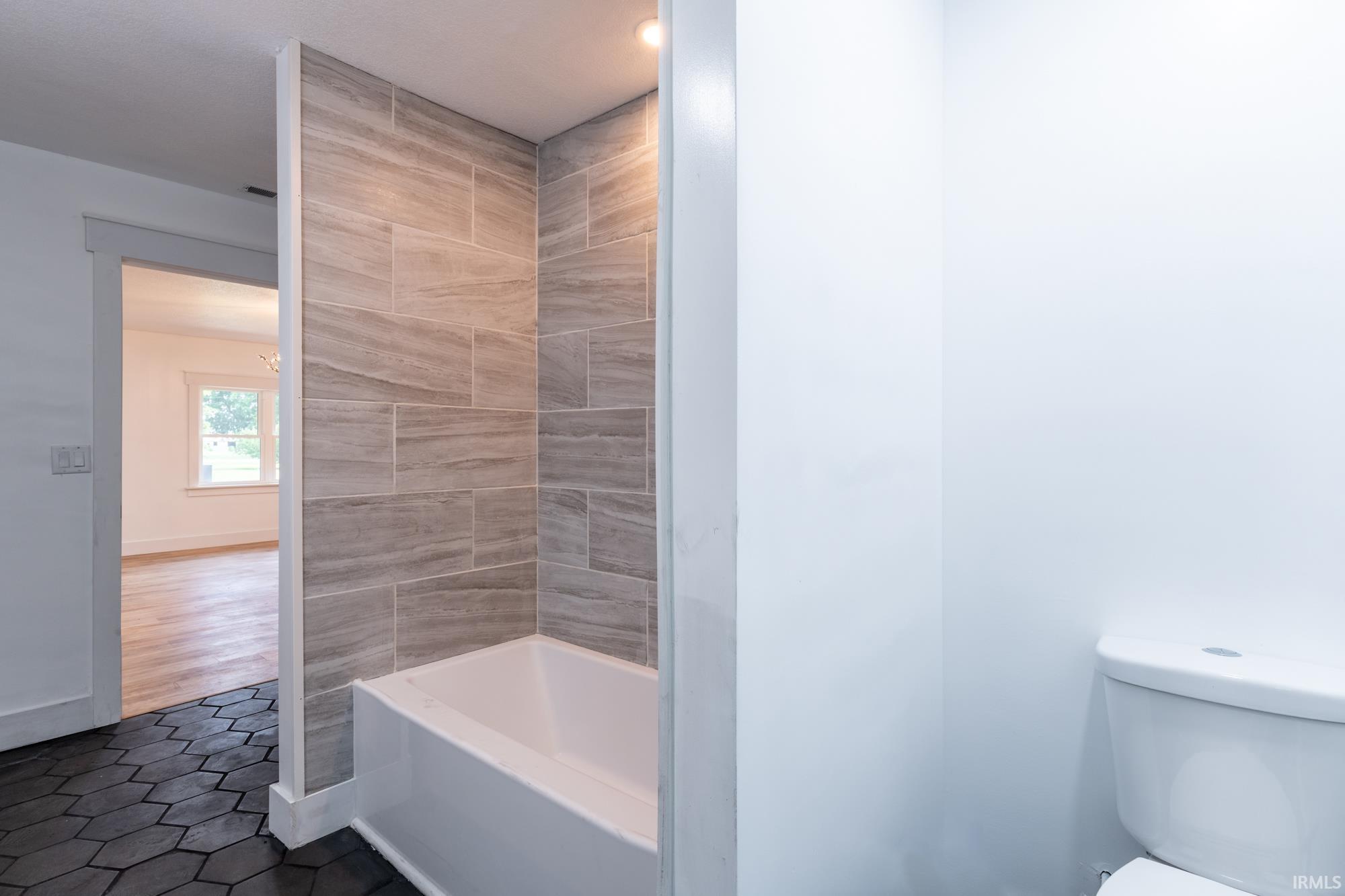 Bathroom featuring a white bathtub, light-toned rectangular wall tiling, recessed lighting, and dark hexagonal floor tiling