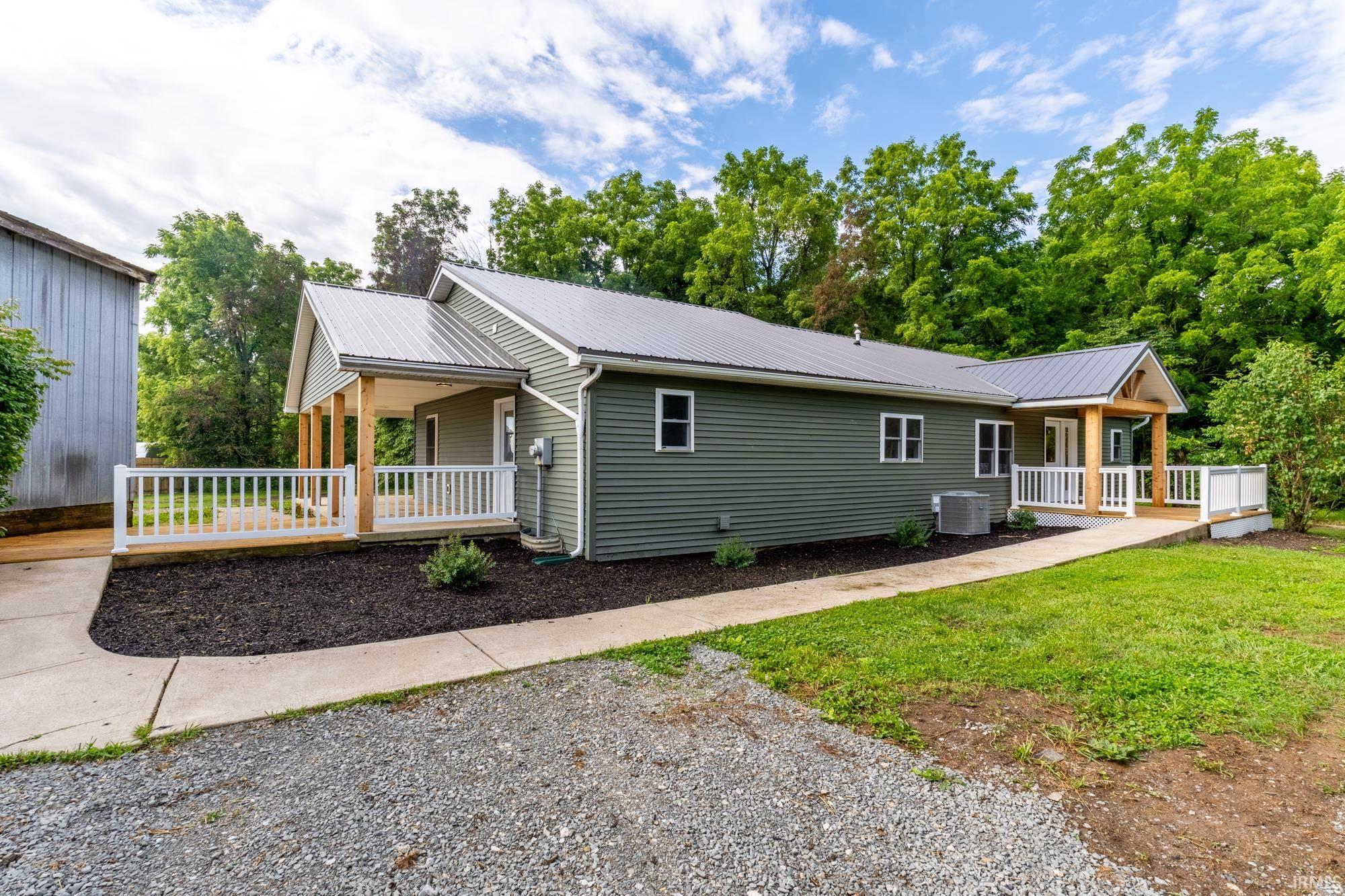 Single-story residence featuring green siding, a metal roof, and a gravel driveway