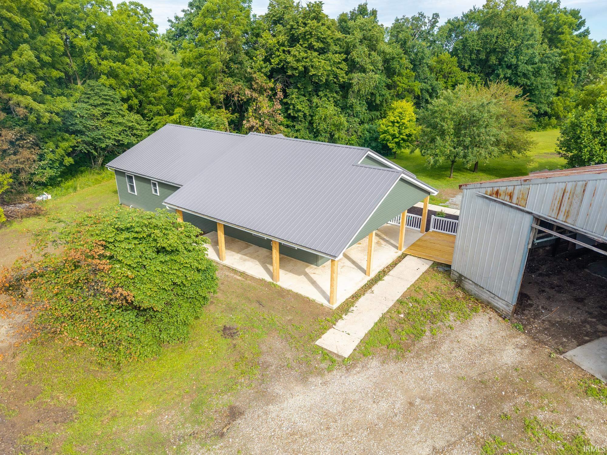 Modern farmhouse-style residence featuring a gray metal roof, olive green siding, a covered porch with natural wood columns, and a dedicated gravel driveway