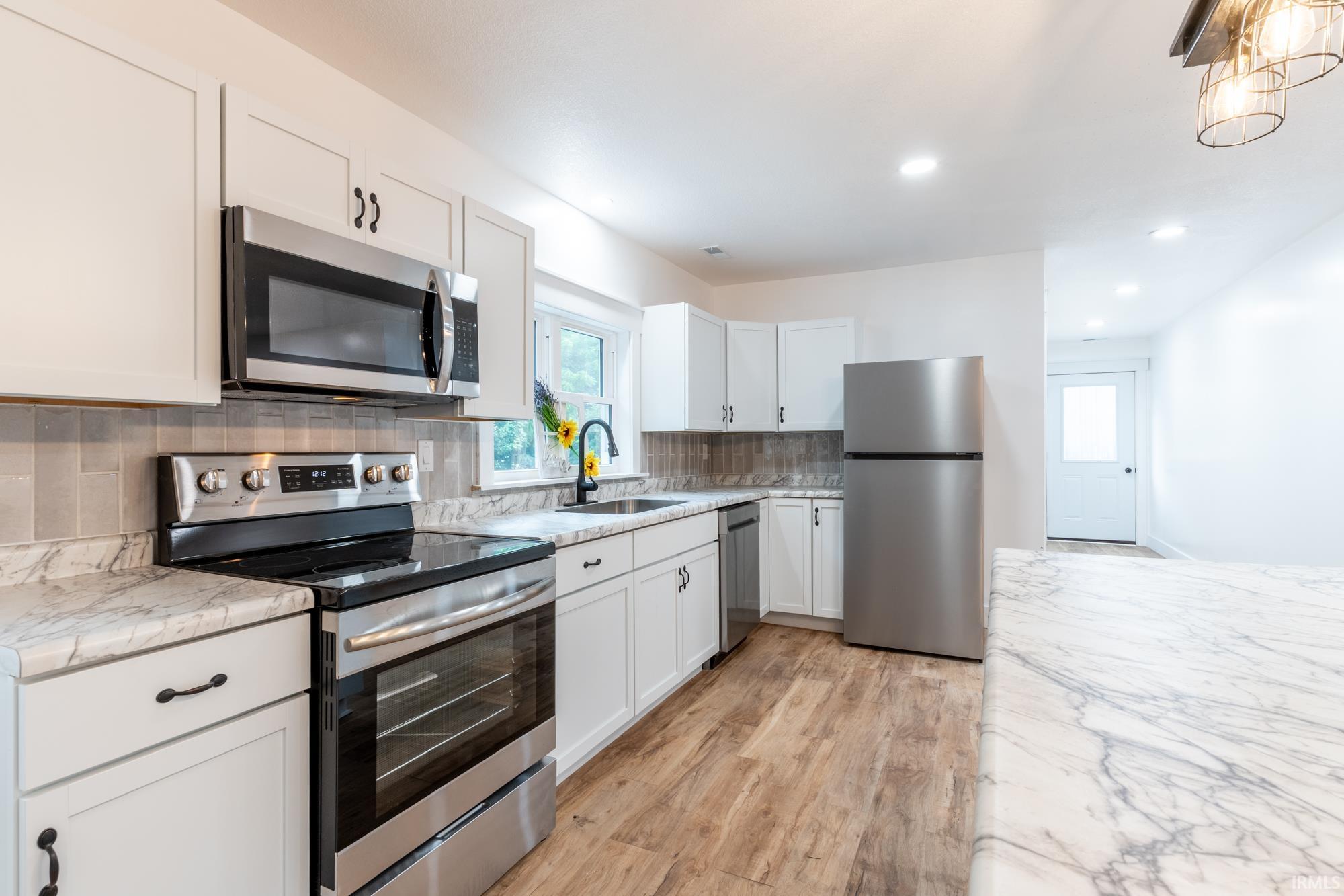 White cabinetry kitchen featuring stainless steel appliances, marble-patterned countertops, a tile backsplash, and wood-finish flooring