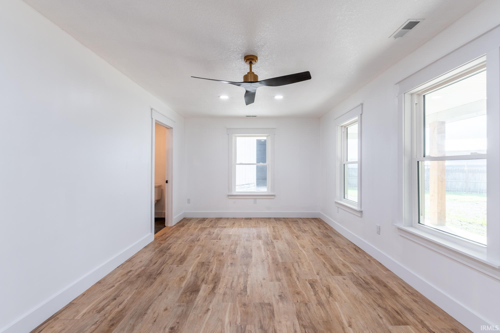 Bright room featuring wood-finish flooring, crisp white walls, and multiple windows with white trim