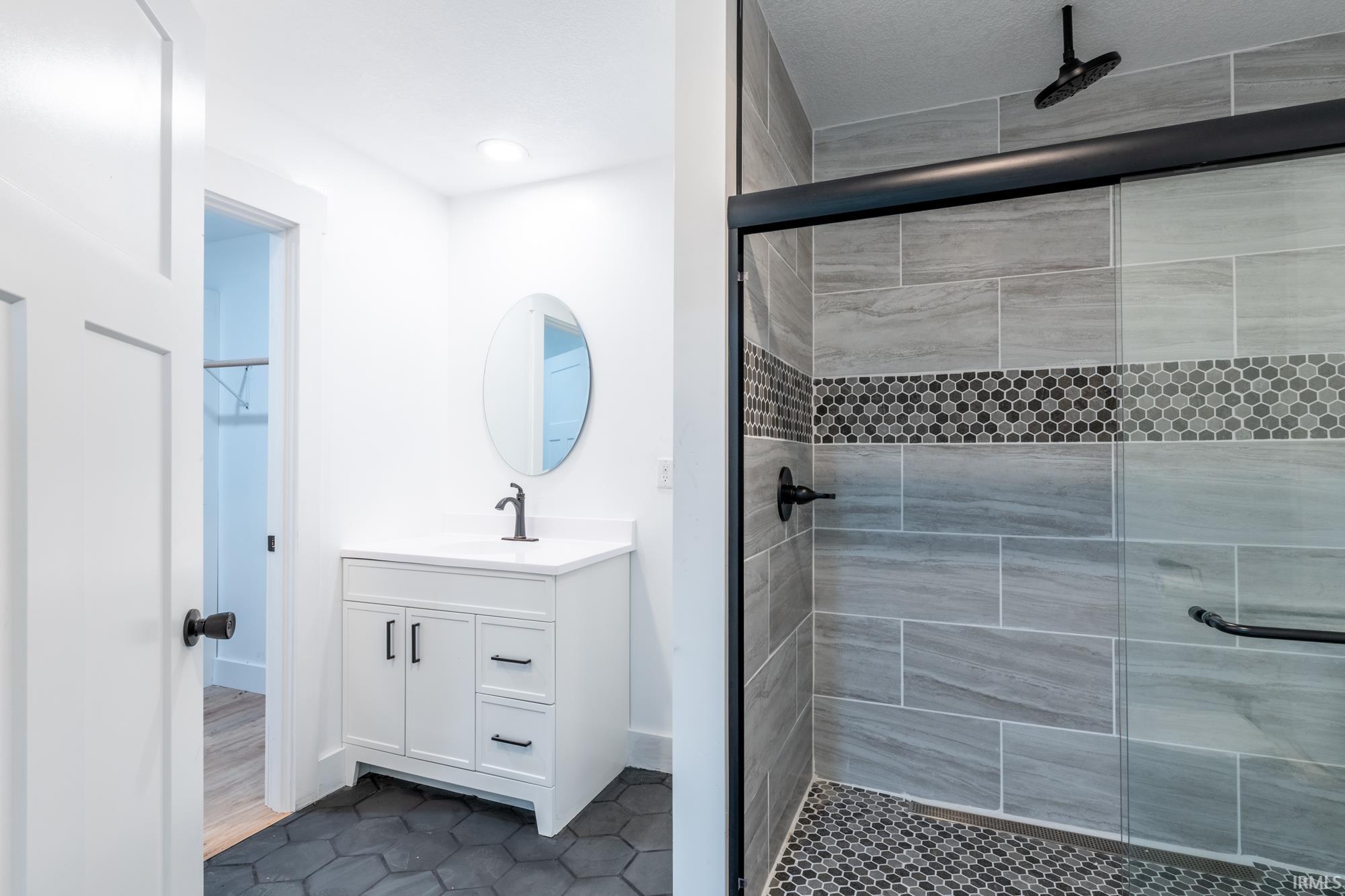 Contemporary bathroom featuring a black-framed glass shower enclosure, large format gray tile shower walls, and a decorative hexagonal mosaic tile band