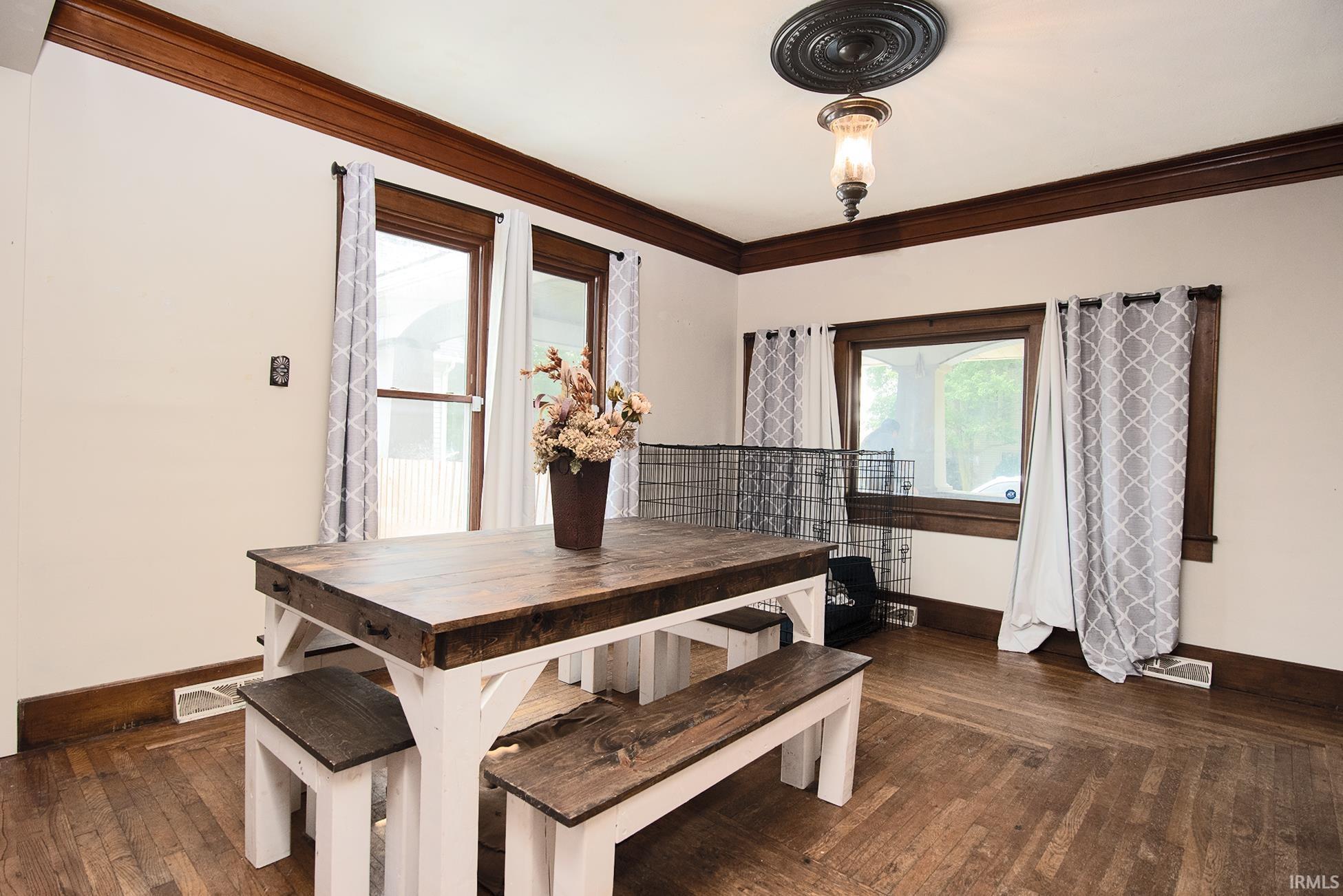 Room featuring wood-finish flooring, dark wood trim, crown molding, and a decorative ceiling medallion with an attached light fixture