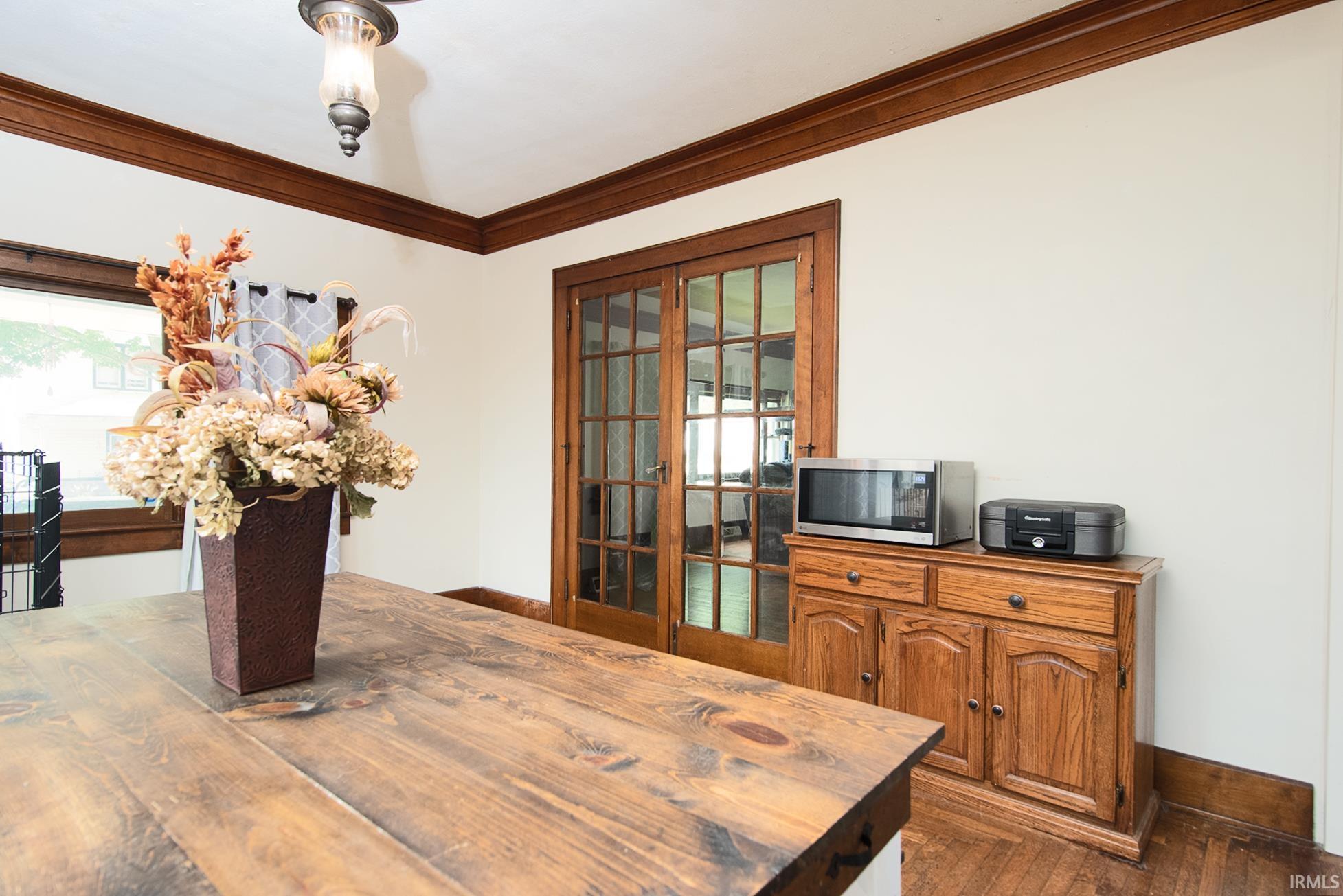 Wood-finish flooring accentuating a built-in wood cabinet, French doors, and a decorative ceiling light fixture