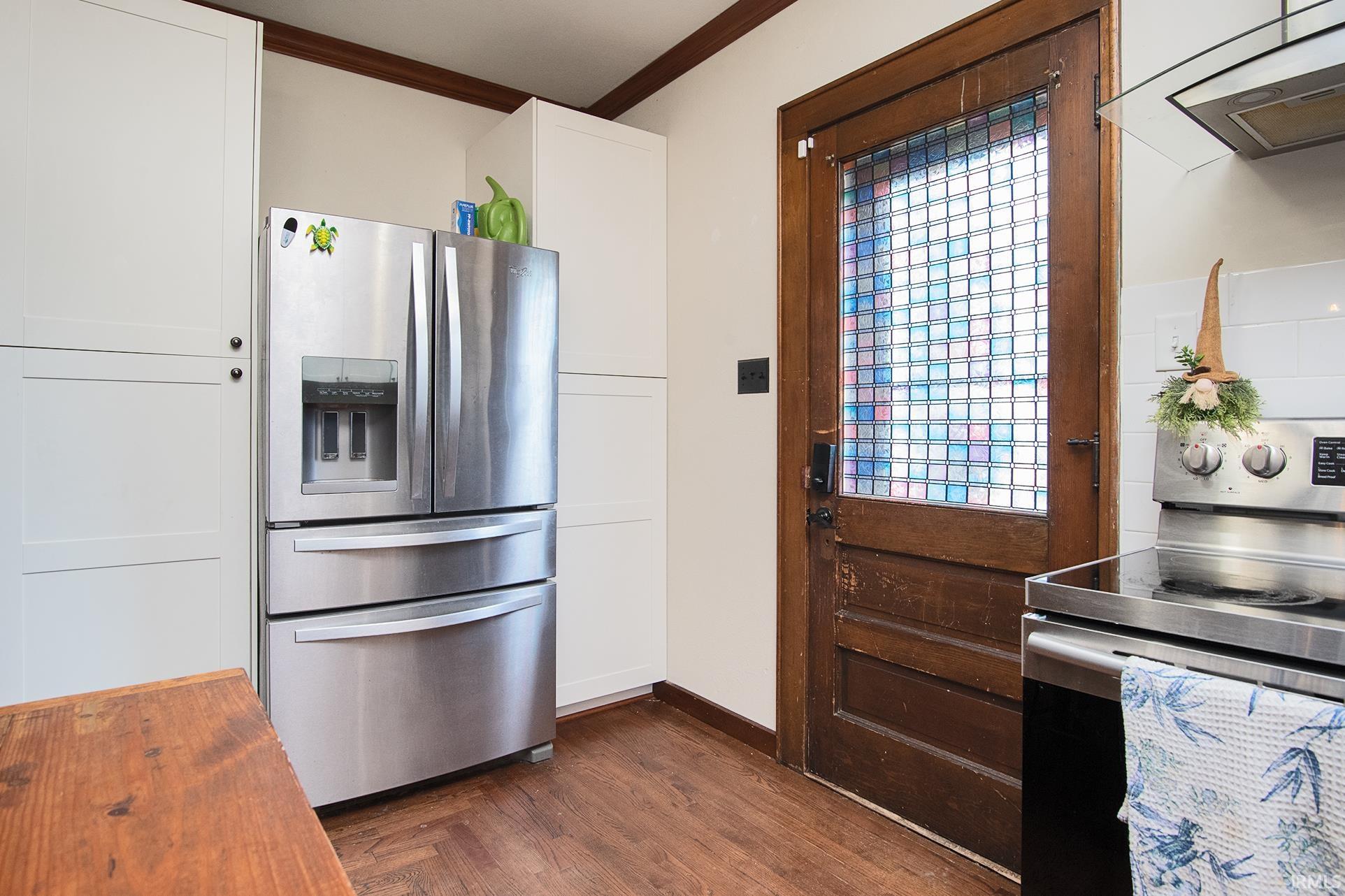Wood-finish flooring complements the white cabinetry and dark wood door with patterned glass
