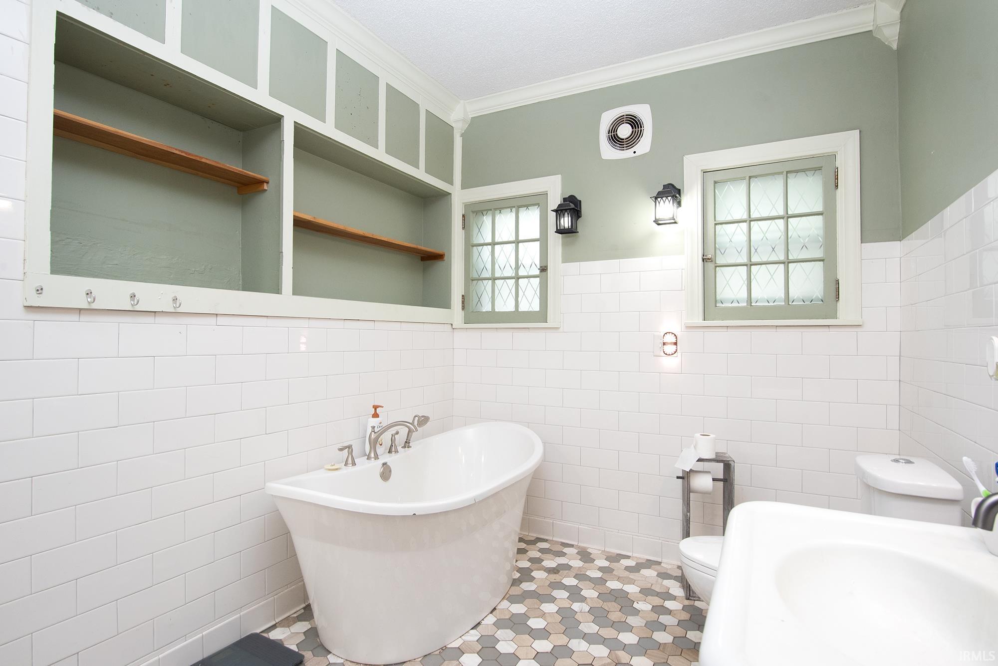 Freestanding soaking tub with chrome fixtures, set against white subway tile wainscoting