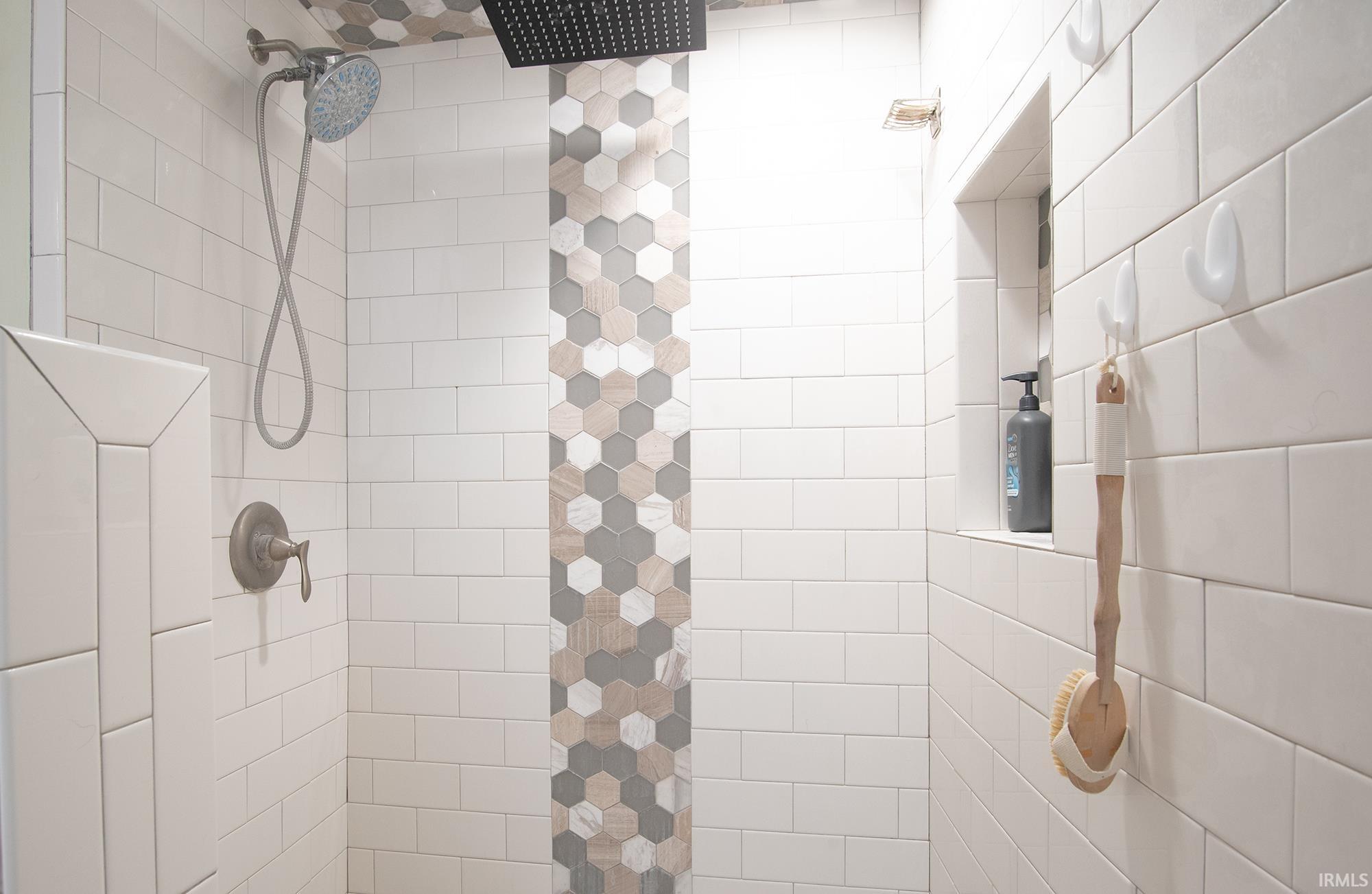 Tiled shower featuring a matte black rain shower head, hand-held shower fixture, and an integrated tiled niche