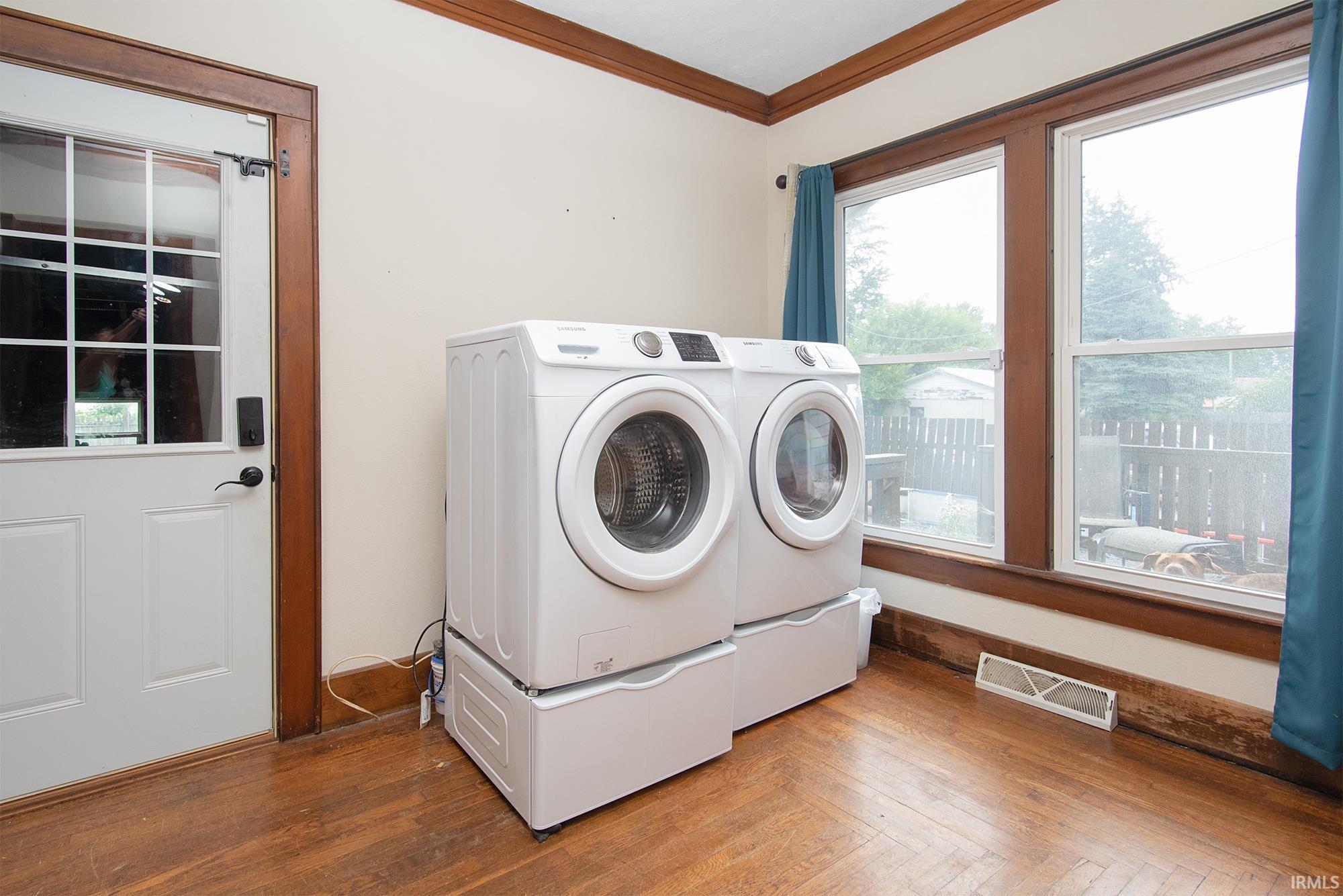 Laundry area featuring wood-finish flooring, two large windows, a white paneled door with glass inserts, and rich wood trim