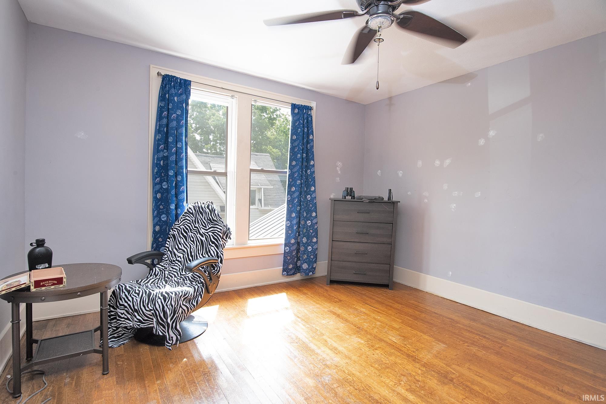 Bright room featuring wood-finish flooring, two large windows, a ceiling fan, and baseboard molding