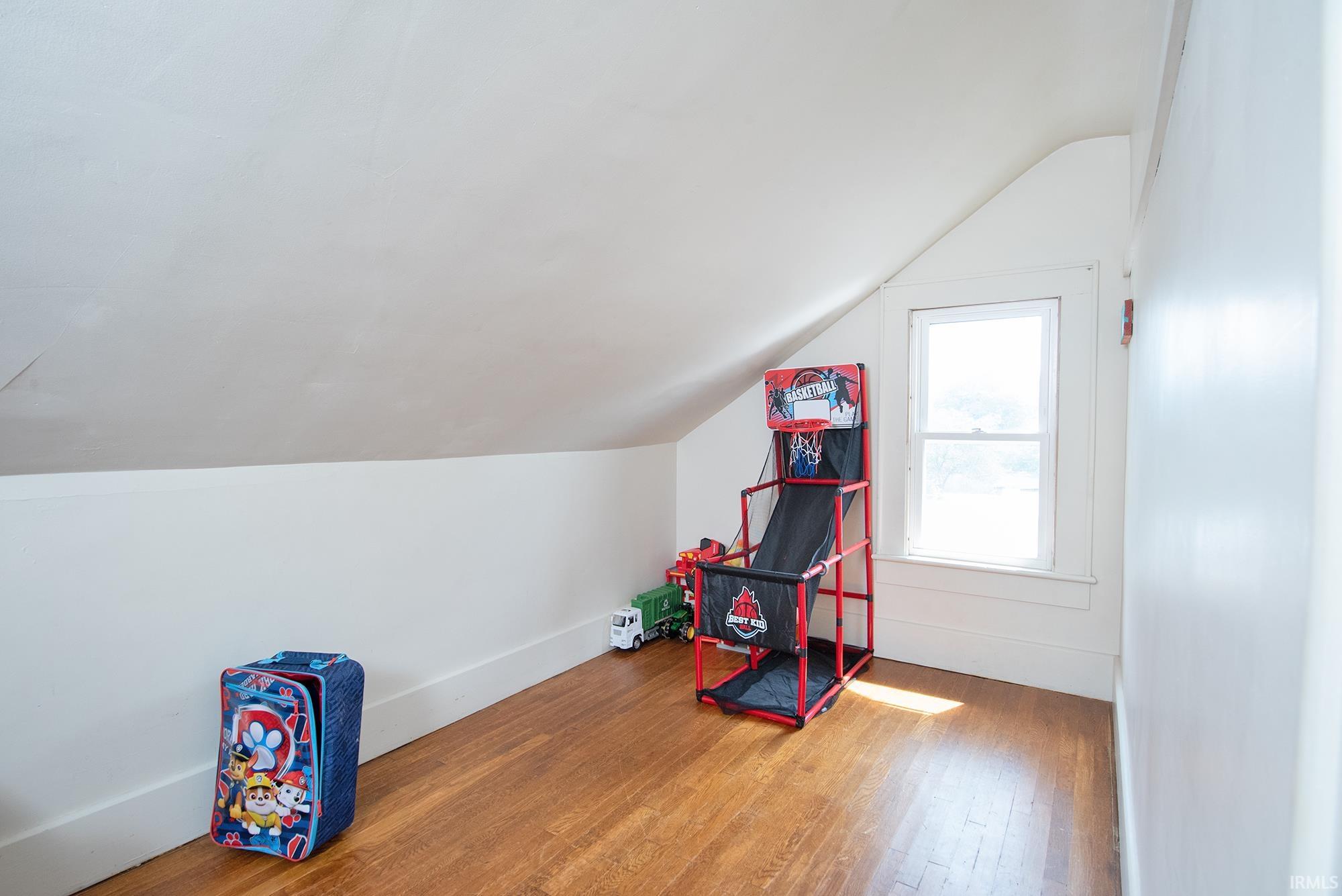Room featuring a sloped ceiling, wood-finish flooring, and a double-hung window with white trim