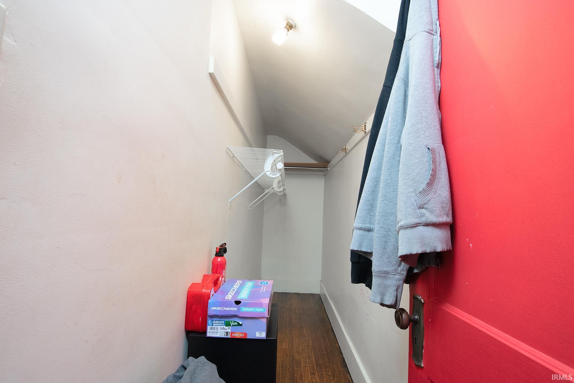 Compact storage area featuring sloped ceilings, wood-finish flooring, and a bright red door with a classic doorknob