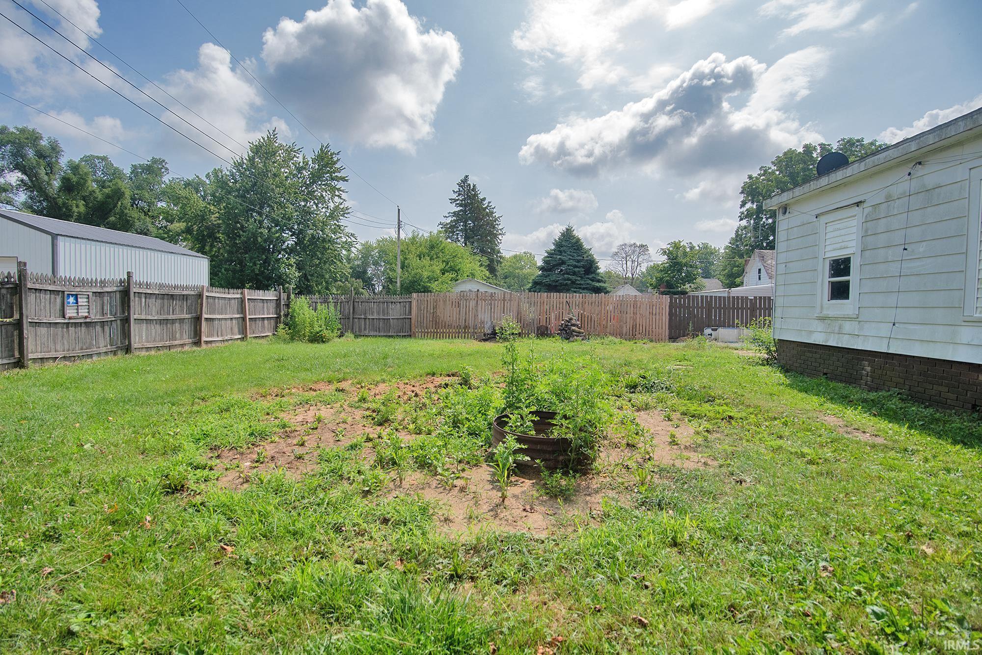 Expansive yard featuring a wooden privacy fence, established trees, and a detached structure in the background