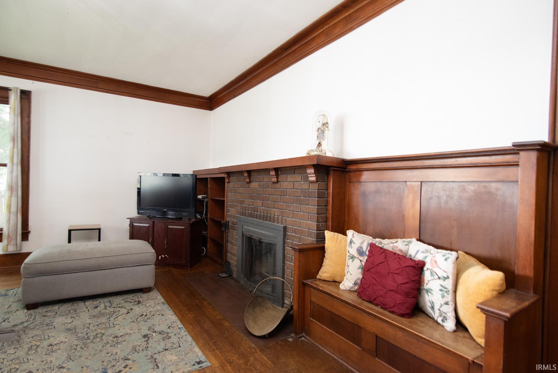 Living area featuring wood-finish flooring, a brick fireplace with a mantel, built-in shelving, extensive wood trim, and a built-in wooden bench