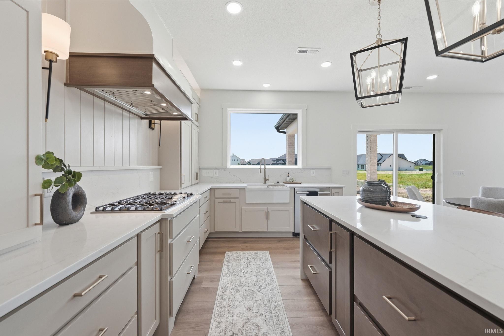 Spacious kitchen featuring an expansive island with a white countertop, a gas range with a custom wood-accented range hood, recessed lighting, and wood-finish flooring