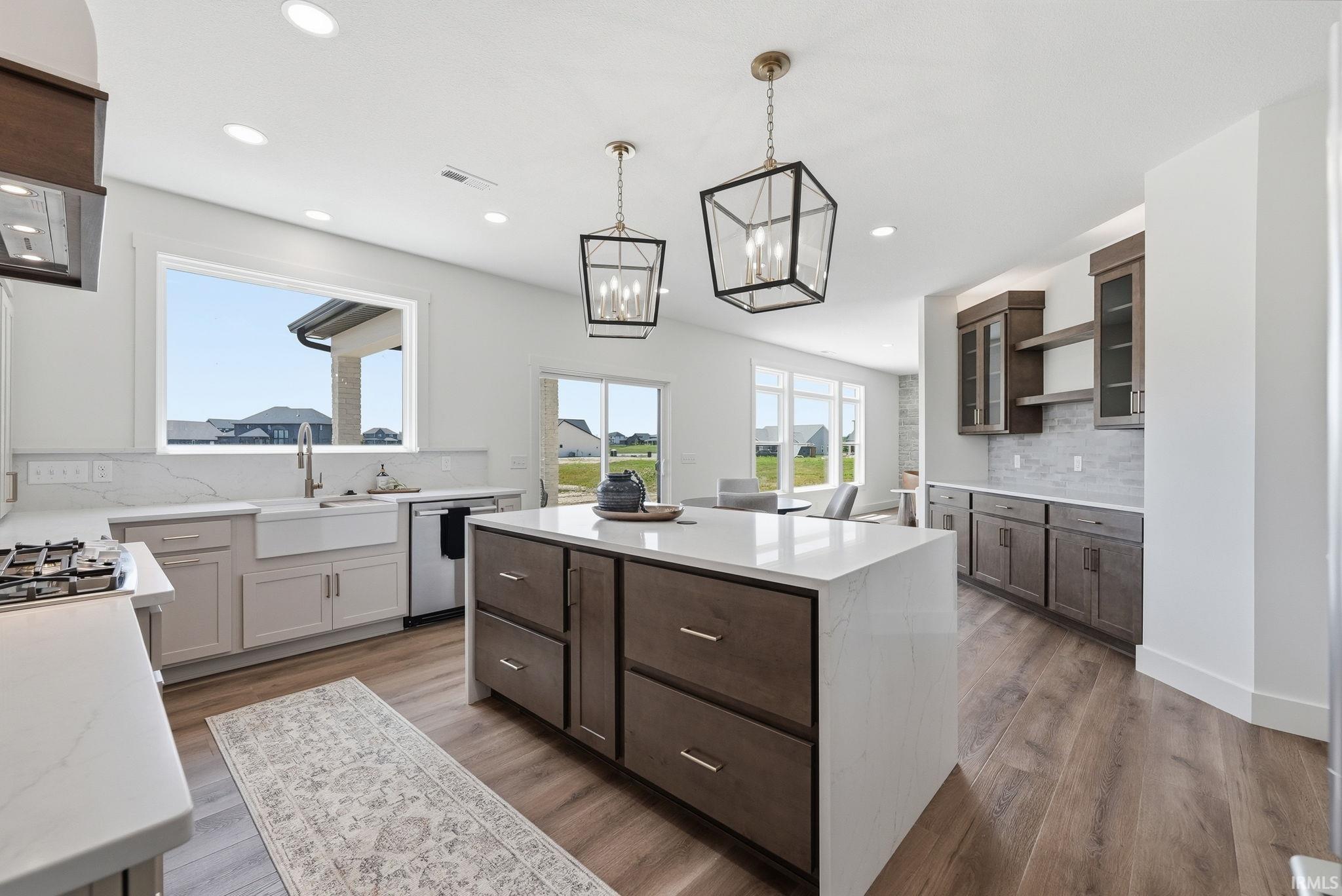Spacious kitchen featuring a large central island, white countertops, wood-finish flooring, recessed lighting, and a built-in dry bar with open shelving