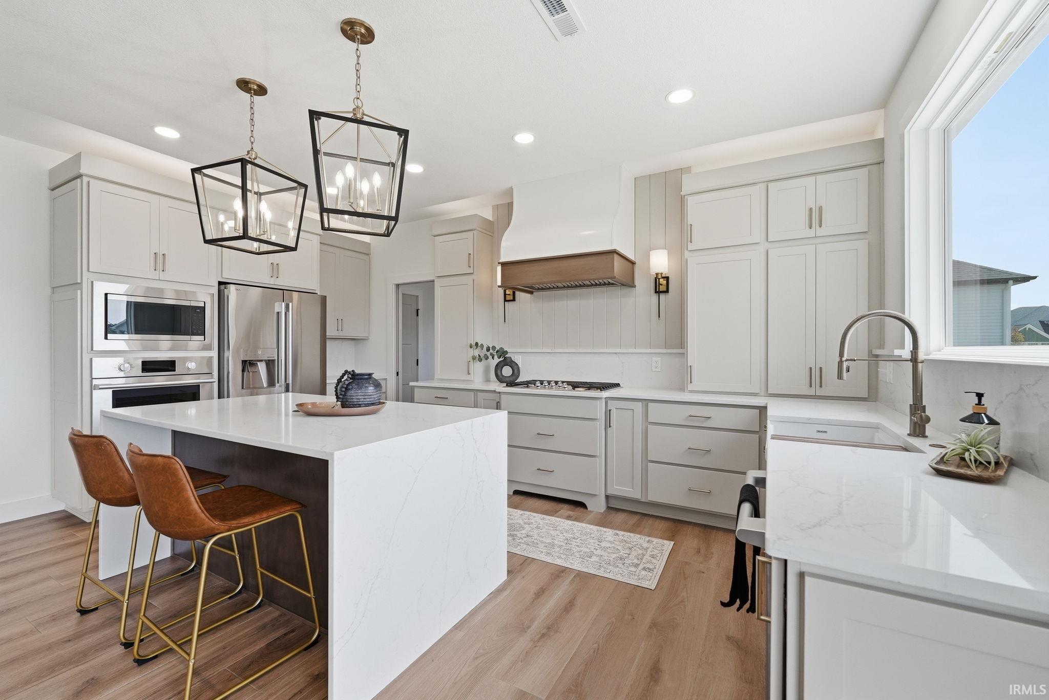 Kitchen with light wood-finish flooring, white cabinetry, integrated stainless steel appliances, a center island with a white countertop, and two black-framed pendant lights