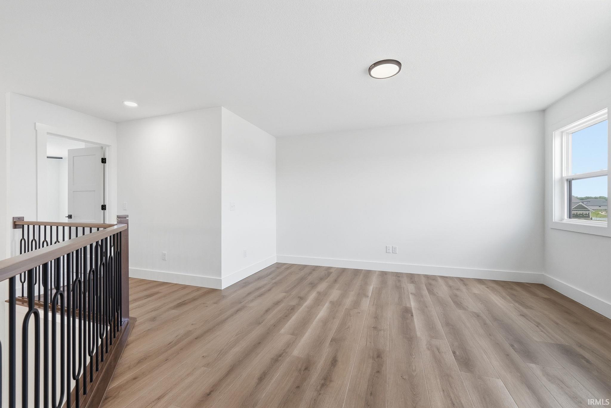 Spacious loft area featuring wood-finish flooring, white walls, and a contemporary ceiling light fixture