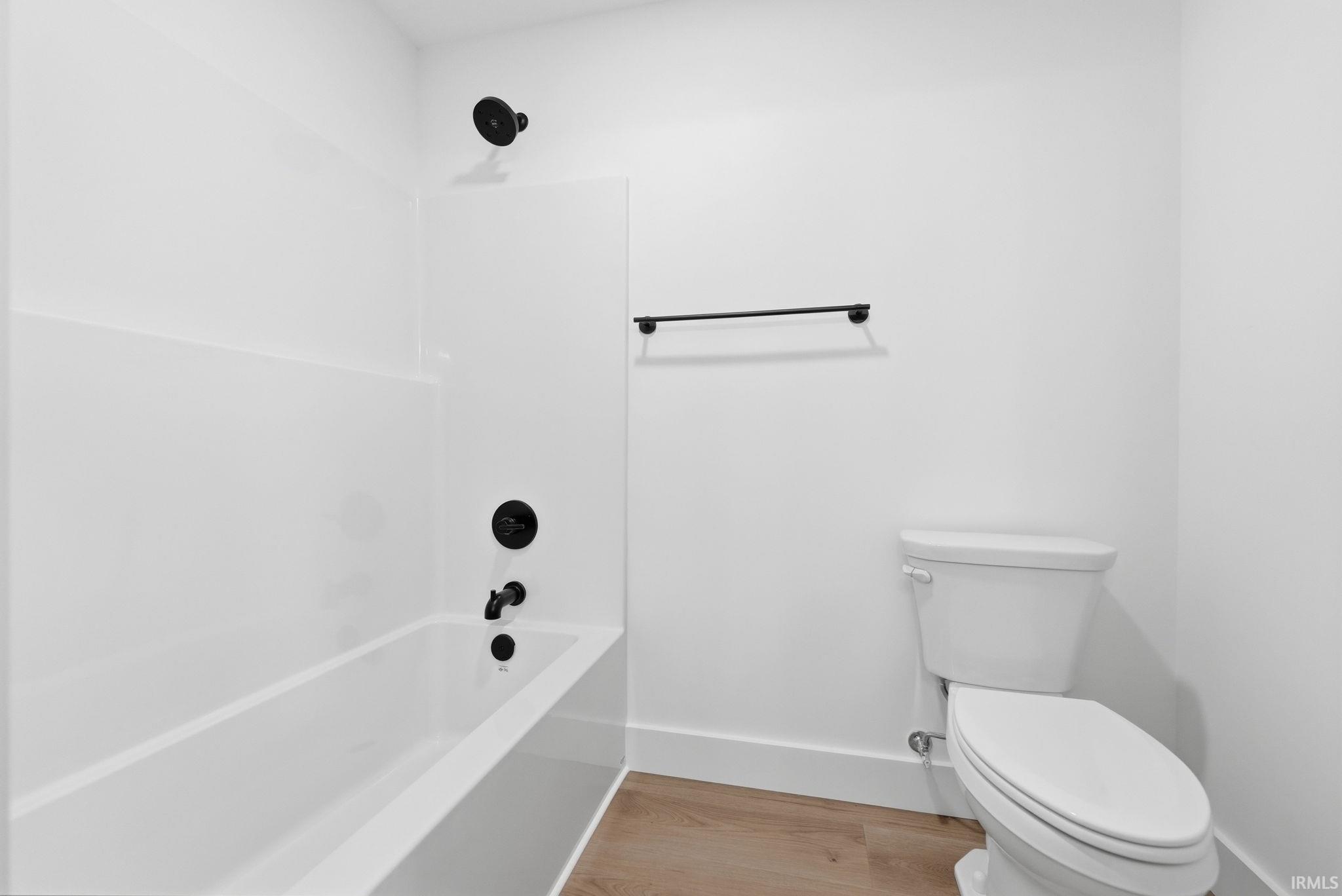 Bathroom featuring a white bathtub and shower surround with matte black fixtures, a white toilet, and wood-finish flooring