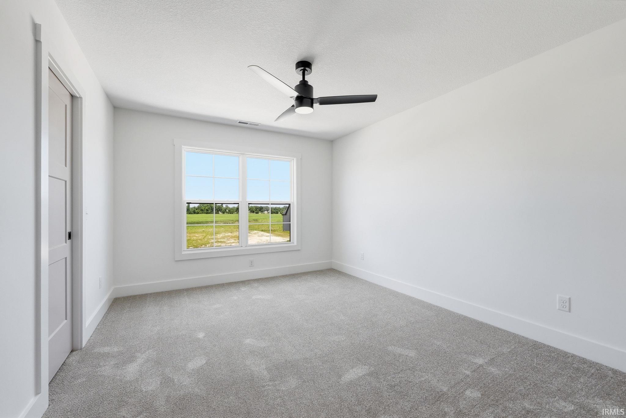 Bright room featuring a large window, plush gray carpet, and a modern black ceiling fan