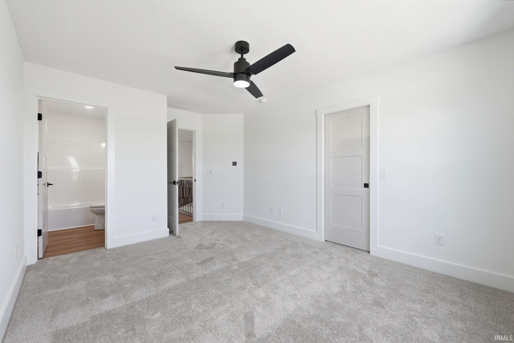 Bright room with light gray carpeting, white walls, and a modern black ceiling fan