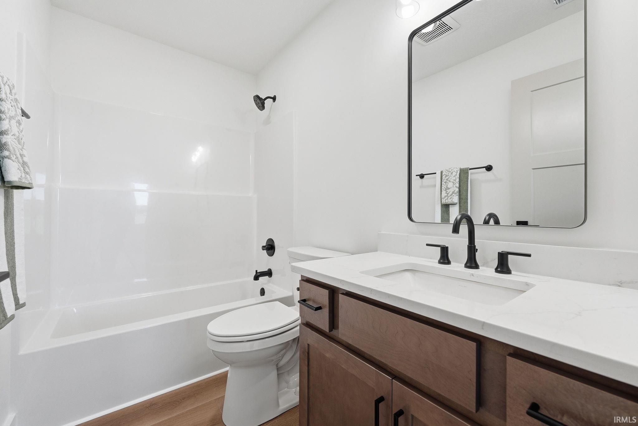 Bathroom featuring a tub/shower combination with black fixtures, wood-finish flooring, a white vanity with an undermount sink, black faucet, and a rectangular black-framed mirror