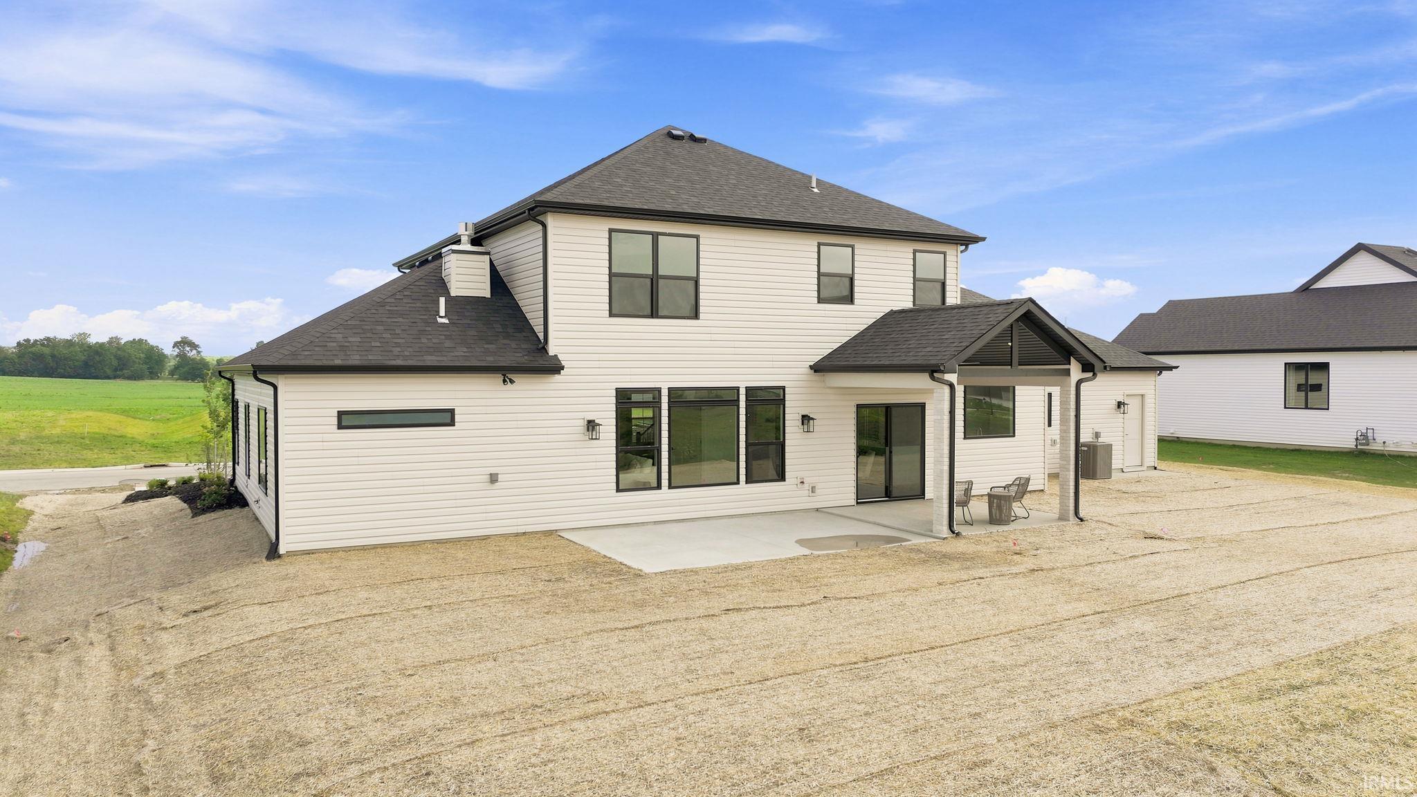 Rear elevation featuring white horizontal siding, dark-framed windows, and a covered patio with a dark roof and columns