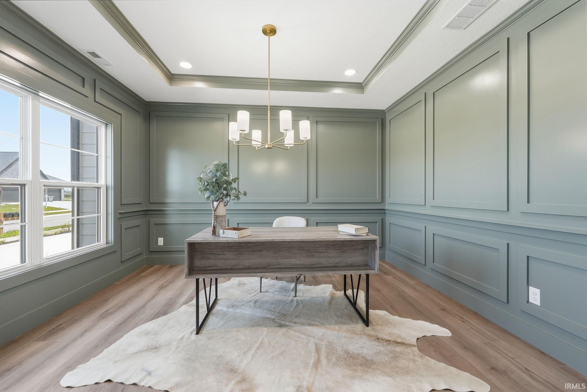 Room featuring extensive wall paneling, a tray ceiling, wood-finish flooring, a contemporary chandelier, and a large double-hung window