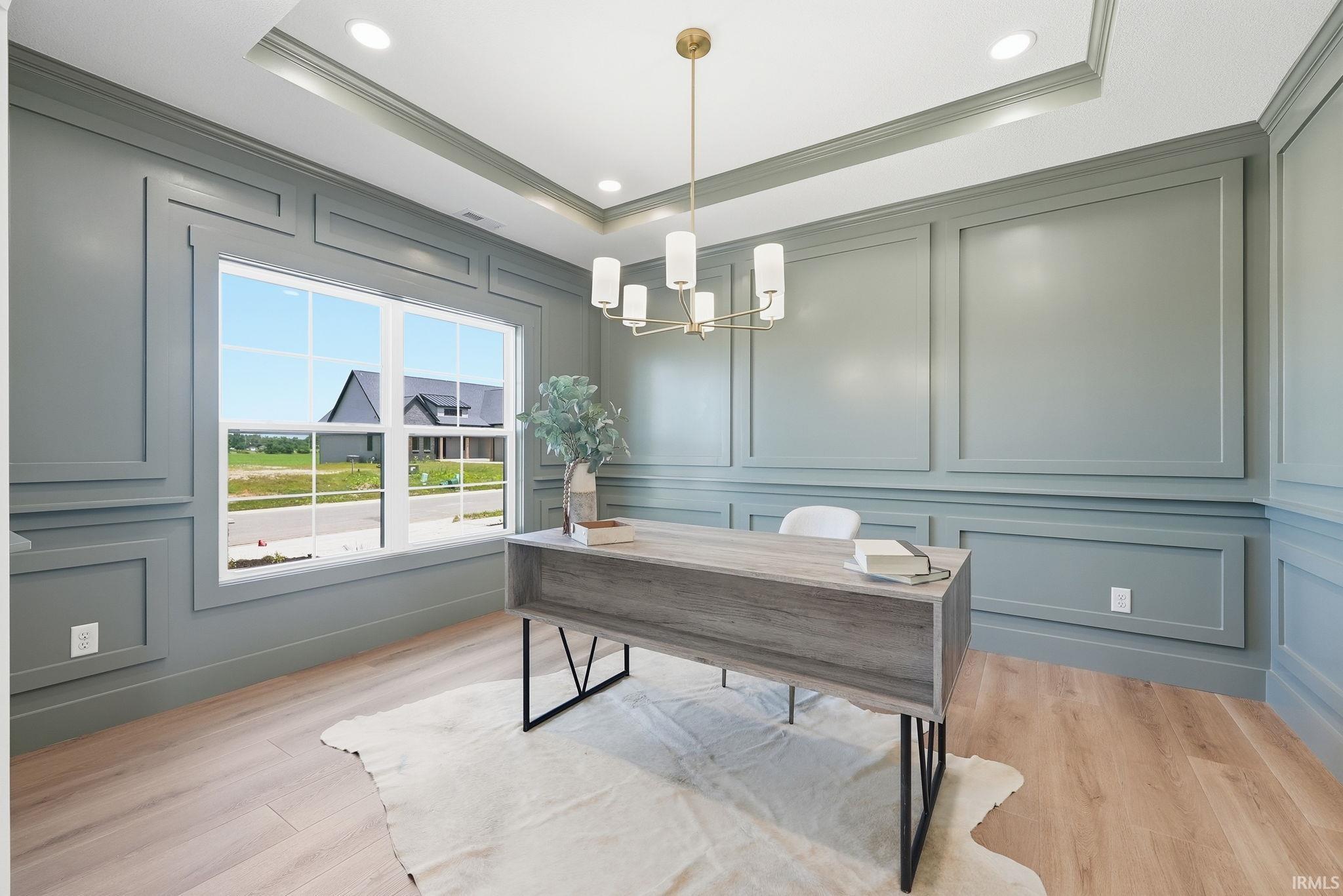 Room featuring detailed wall paneling, light wood-finish flooring, a tray ceiling, recessed lighting, and a contemporary chandelier