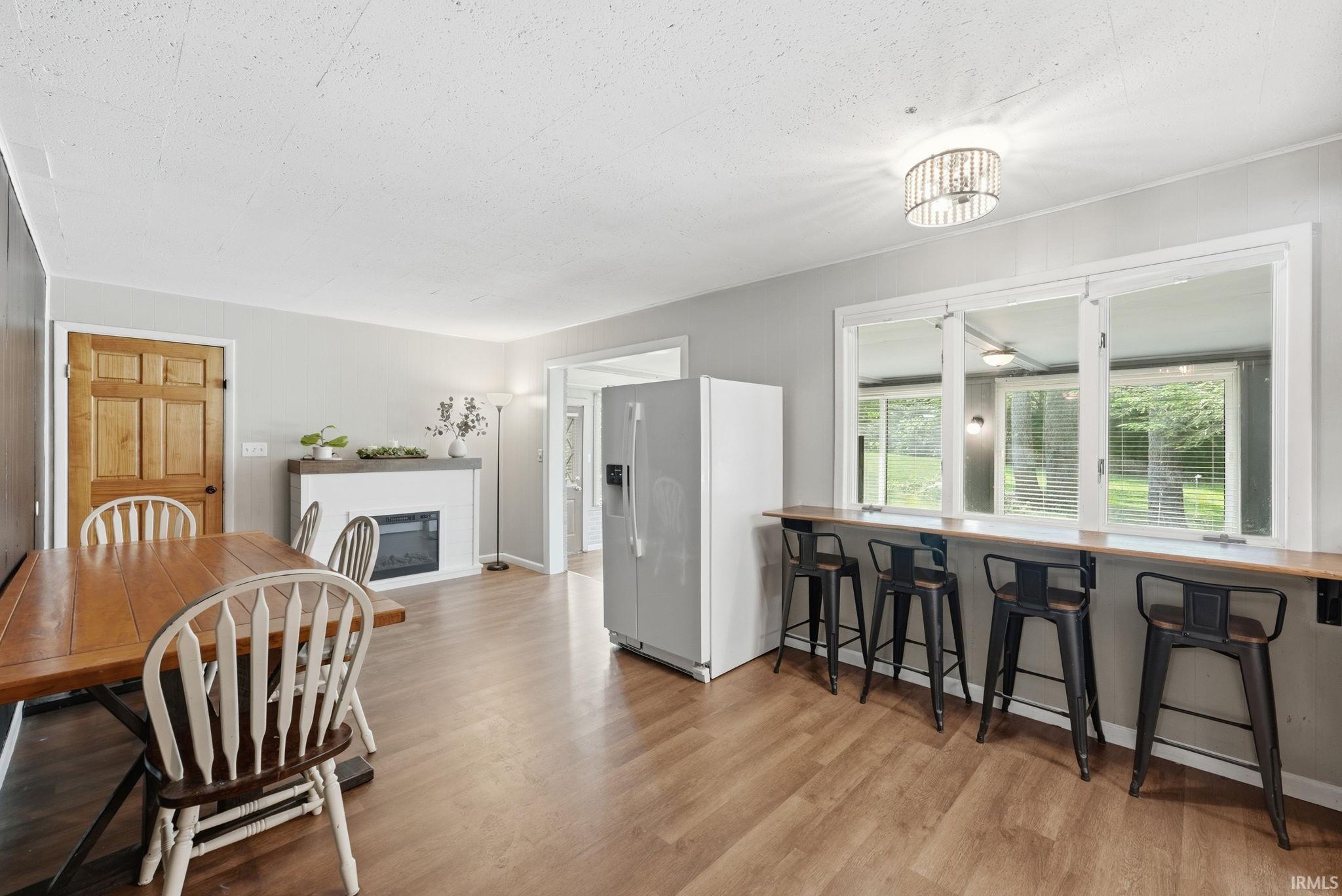 Open-concept living space featuring wood-finish flooring, a modern electric fireplace with a white mantel, and a built-in breakfast bar with seating