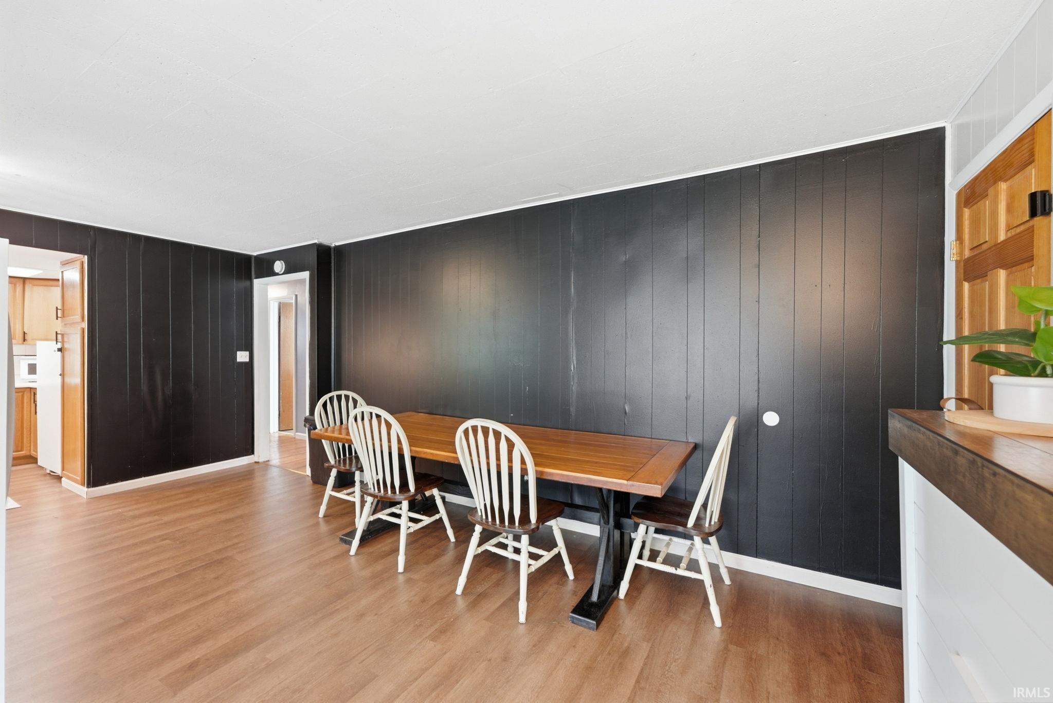 Spacious dining area featuring wood-finish flooring, dark vertical paneling, and an adjacent kitchen entrance
