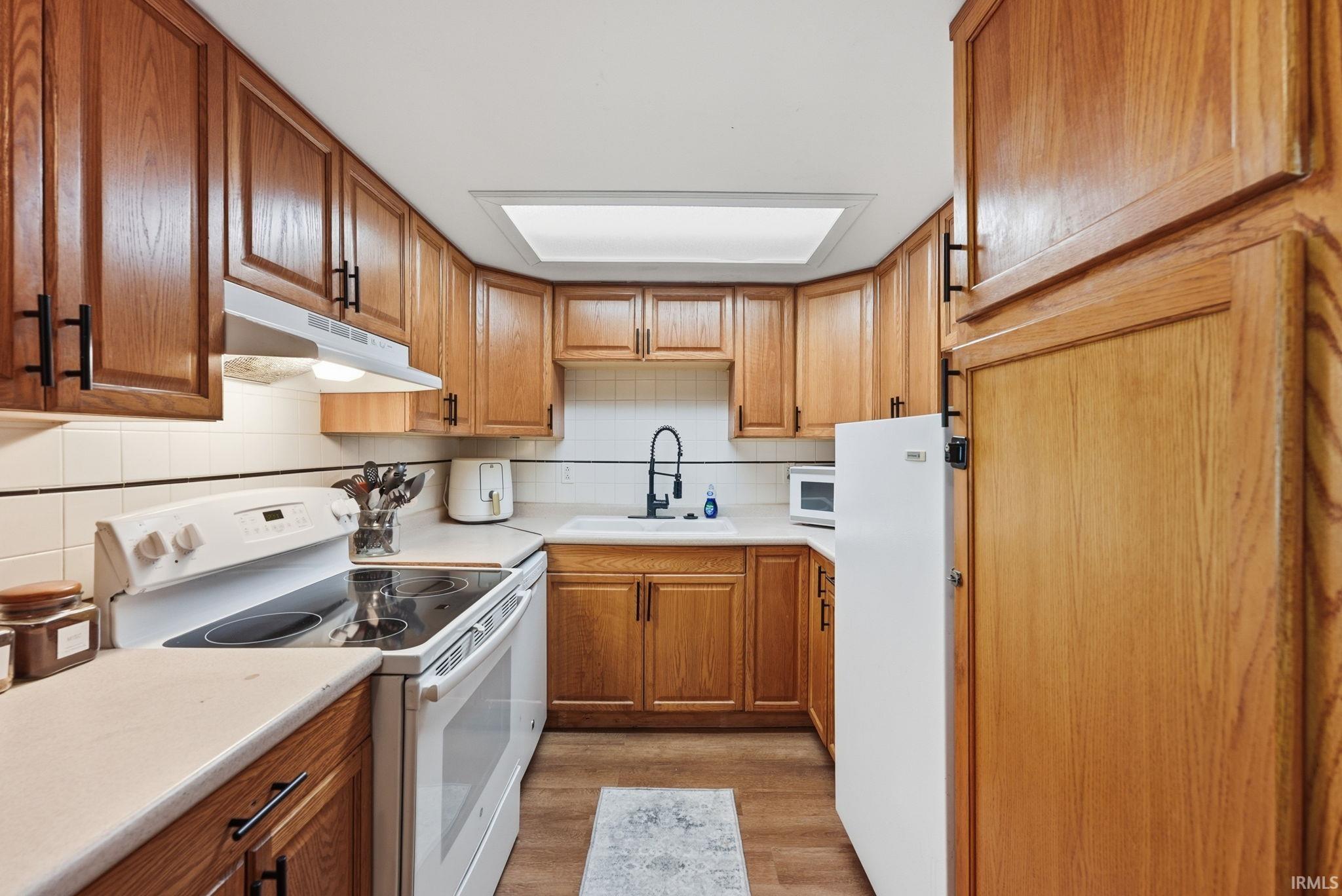 Efficient kitchen featuring abundant wood cabinetry, white appliances, solid surface countertops, and wood-finish flooring