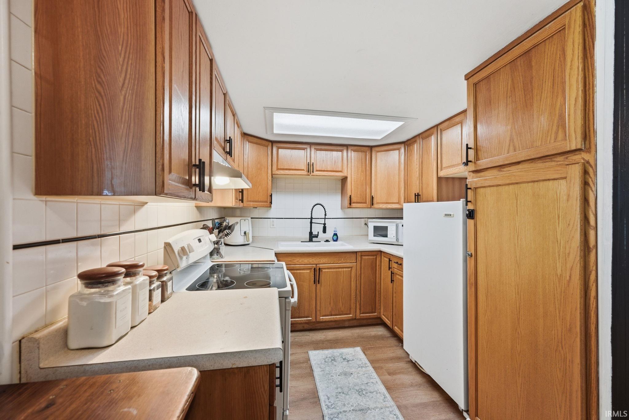 Kitchen featuring extensive wood cabinetry, white tile backsplash, a white sink with a black faucet, and a range with an overhead exhaust fan