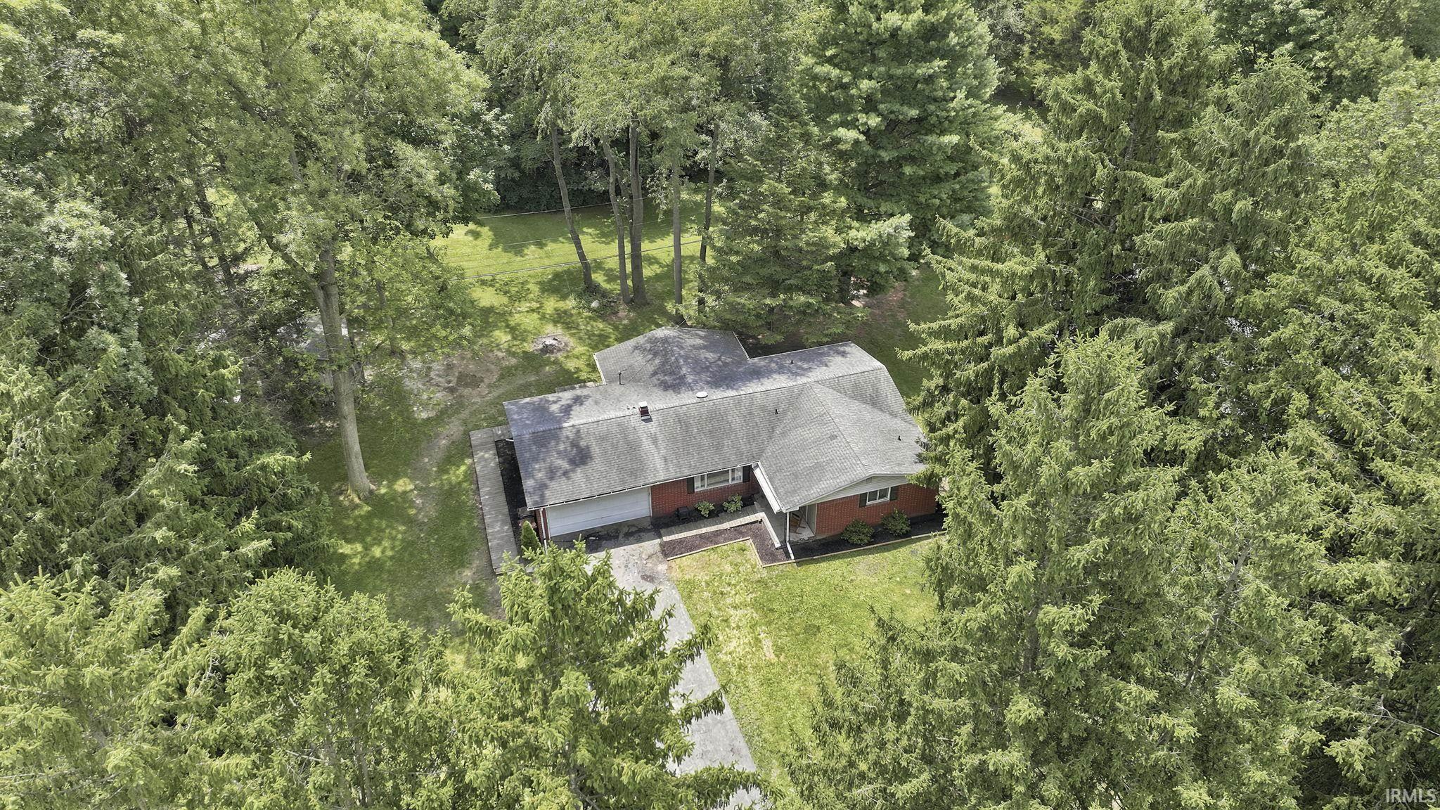Single-story residence set amidst mature trees, featuring red brick siding, a dark shingle roof, and an asphalt driveway