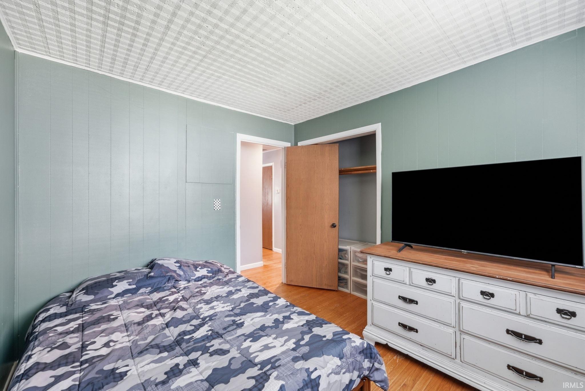 Bedroom featuring paneled walls, wood-finish flooring, a patterned ceiling, and a closet with a built-in storage unit