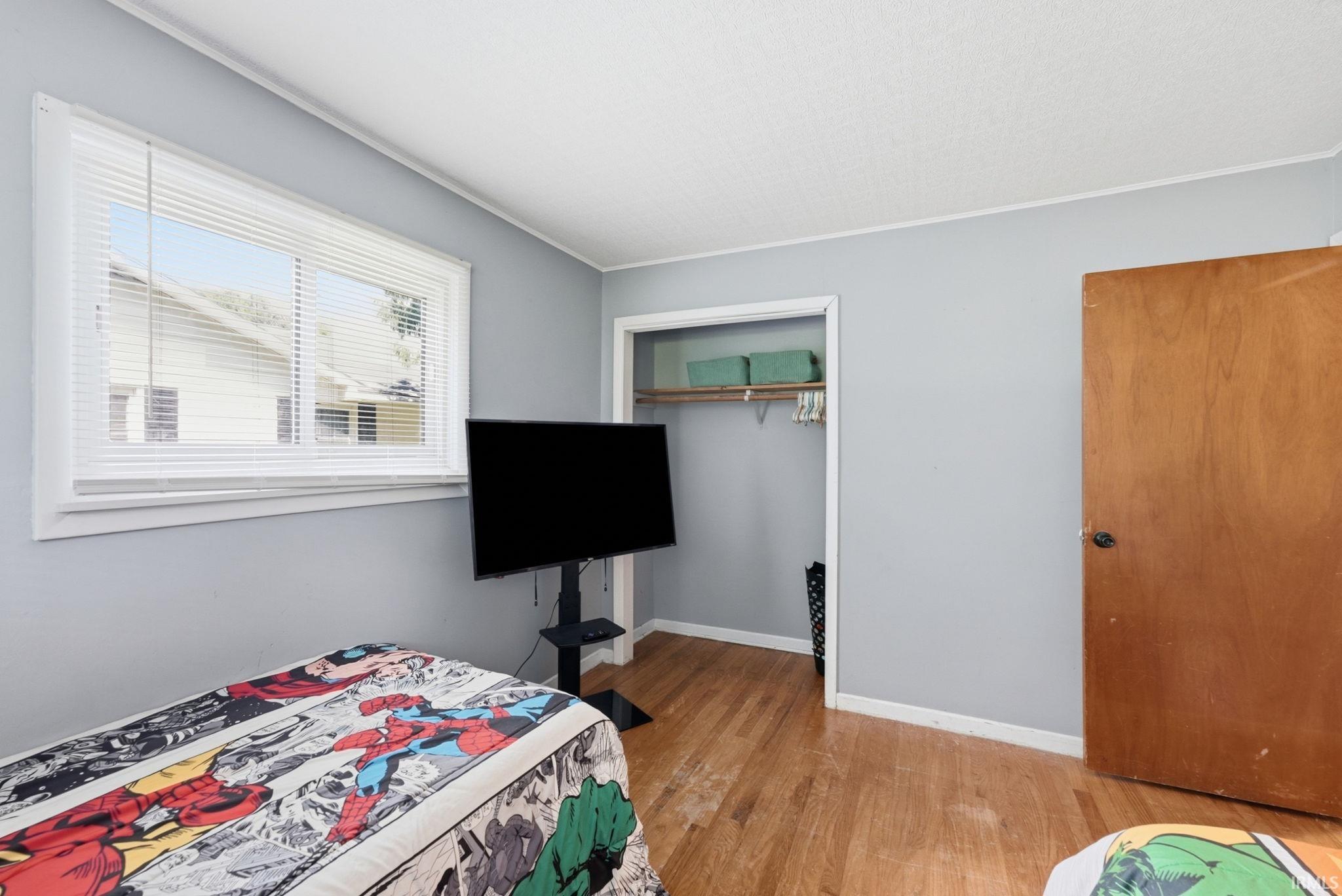Interior room featuring light gray walls, wood-finish flooring, a white-trimmed window with horizontal blinds, and a built-in closet with a wood shelf and hanging rod