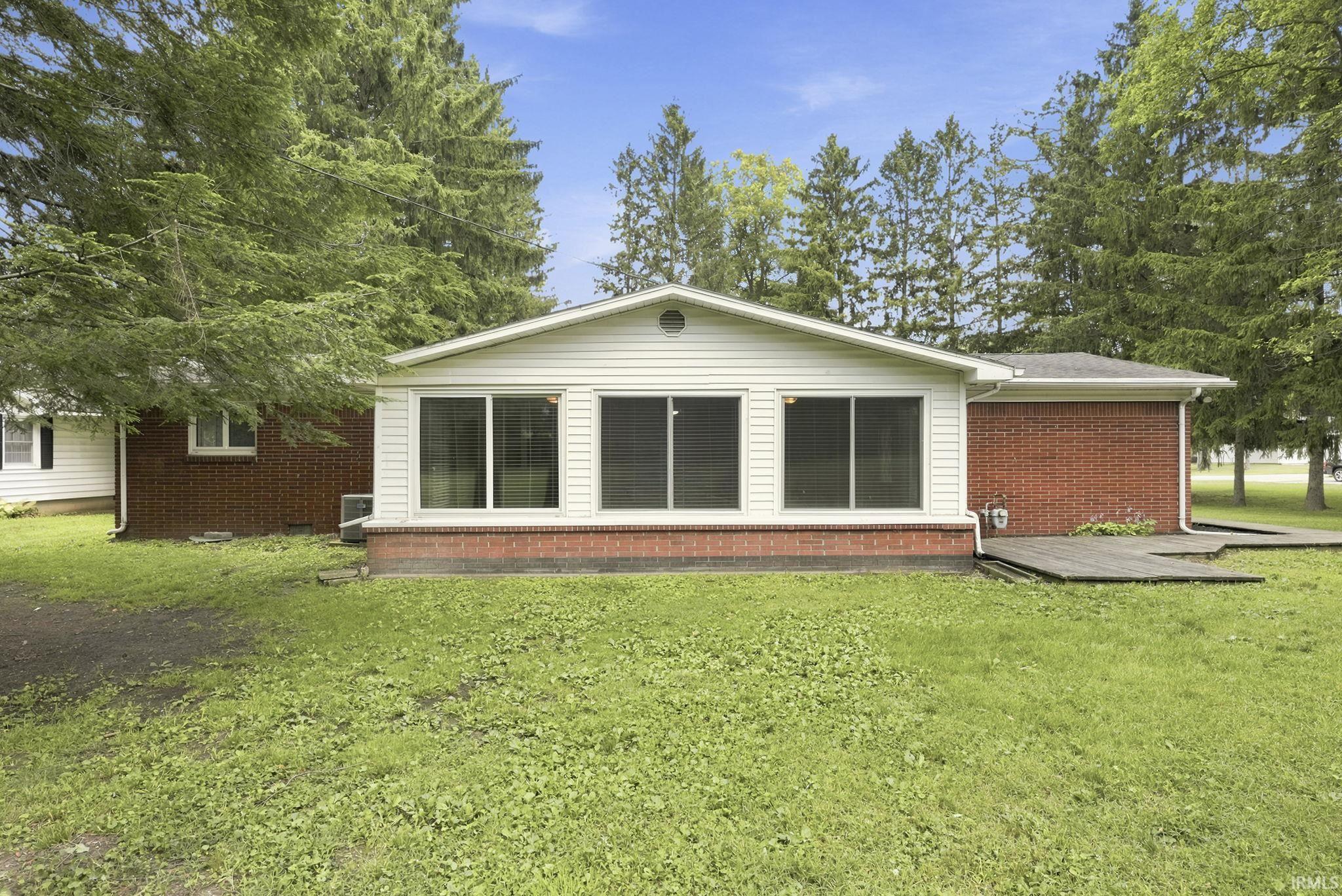 Rear exterior featuring a sunroom addition with large windows, white siding, and a brick foundation
