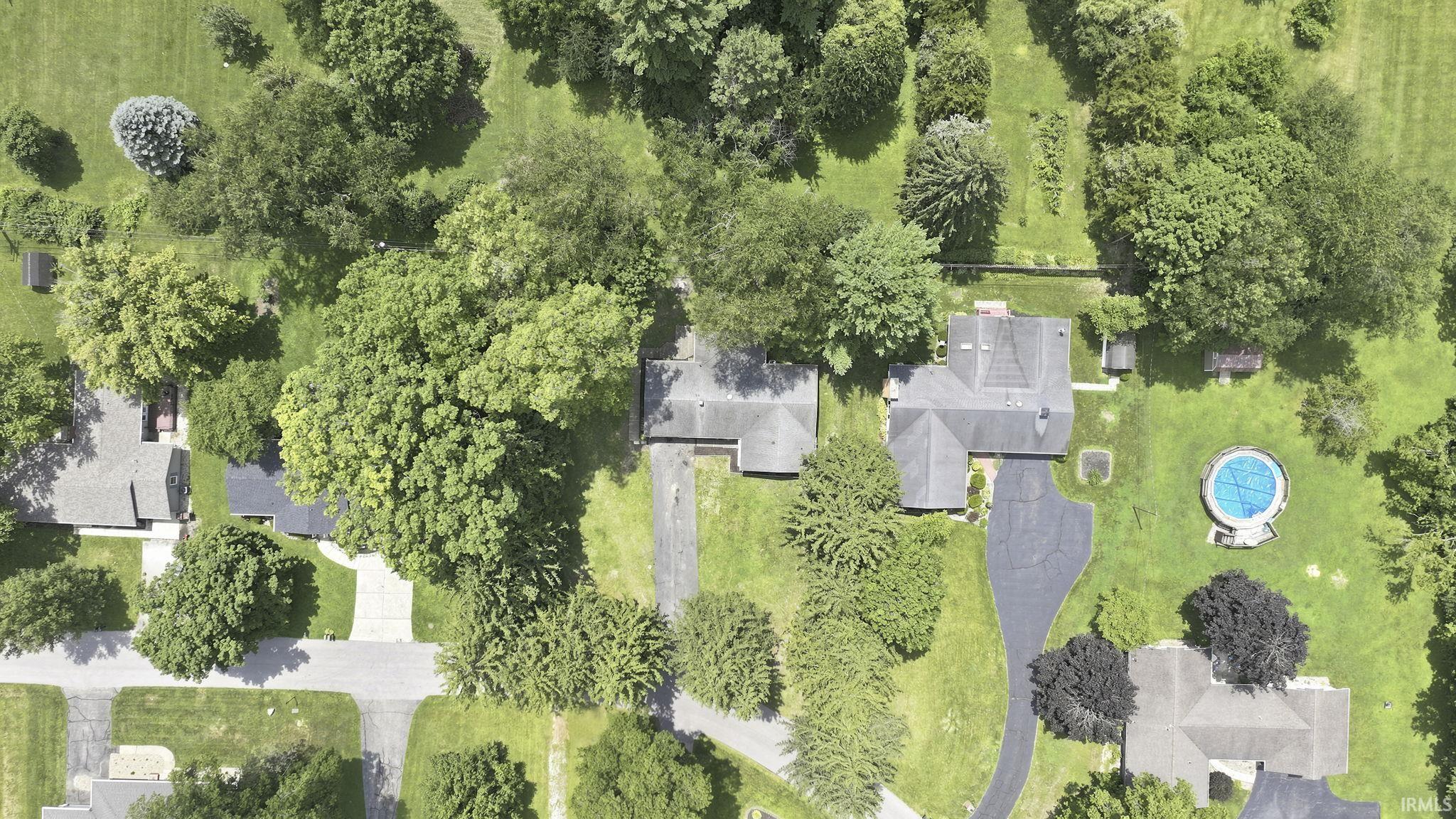Aerial perspective highlighting a residential property with a covered swimming pool, extensive green lawn, and mature trees