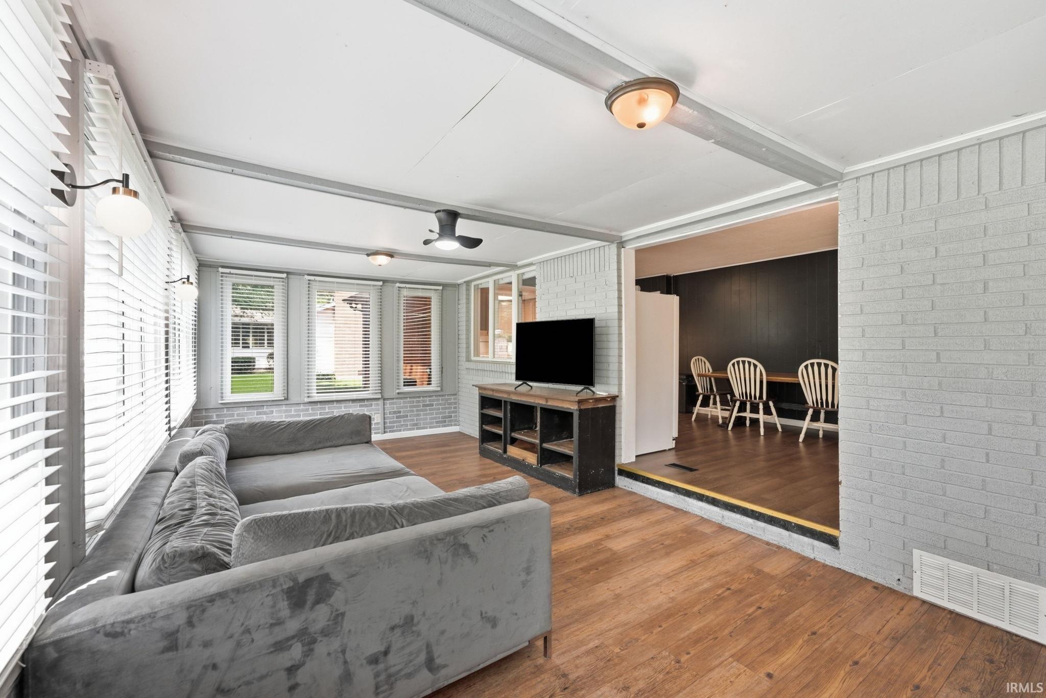 Sunroom with wood-finish flooring, white horizontal blinds, and exposed ceiling beams