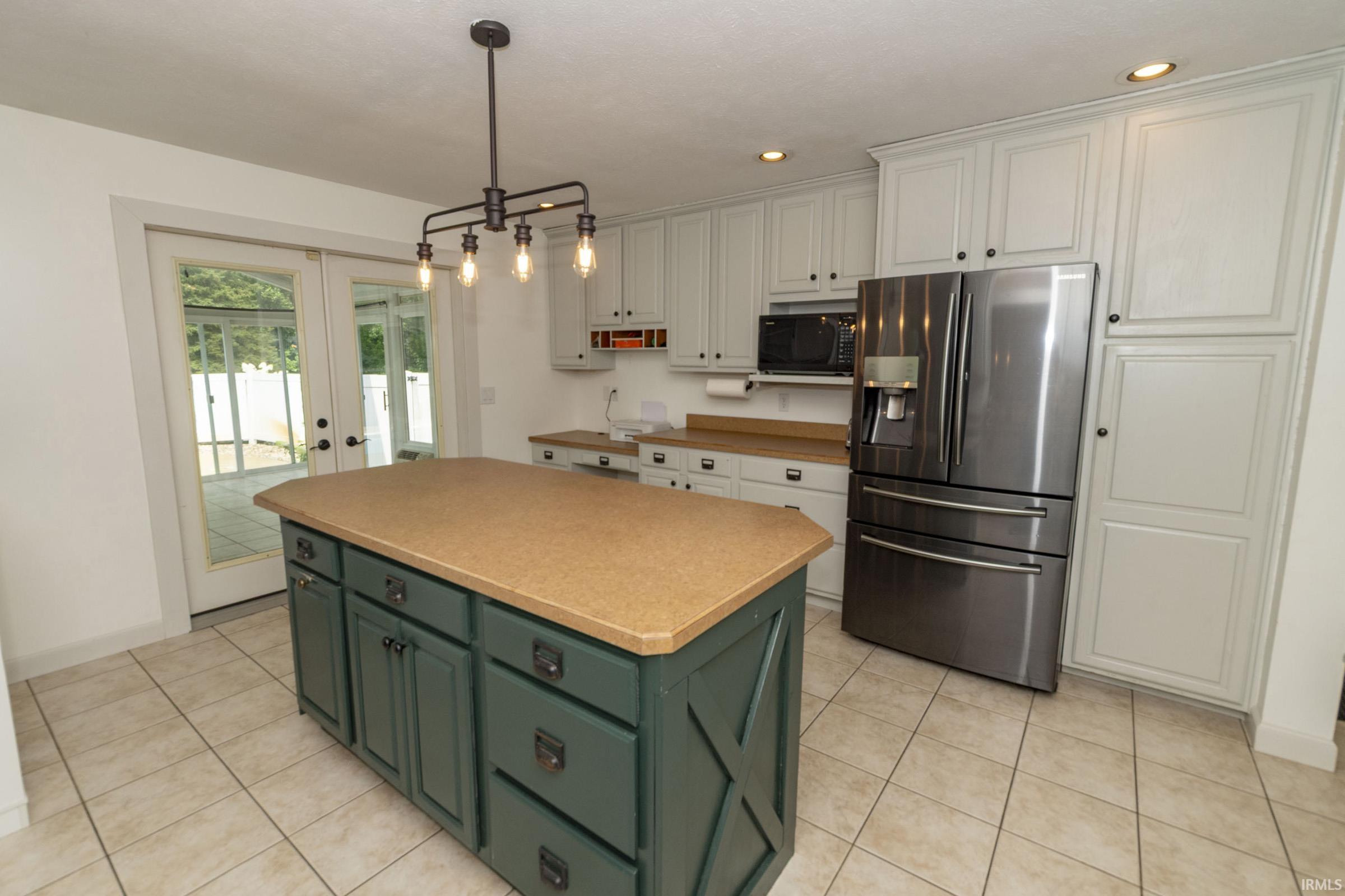 Kitchen featuring a central island with storage, light-toned tiled flooring, light-colored cabinetry, and built-in stainless steel appliances